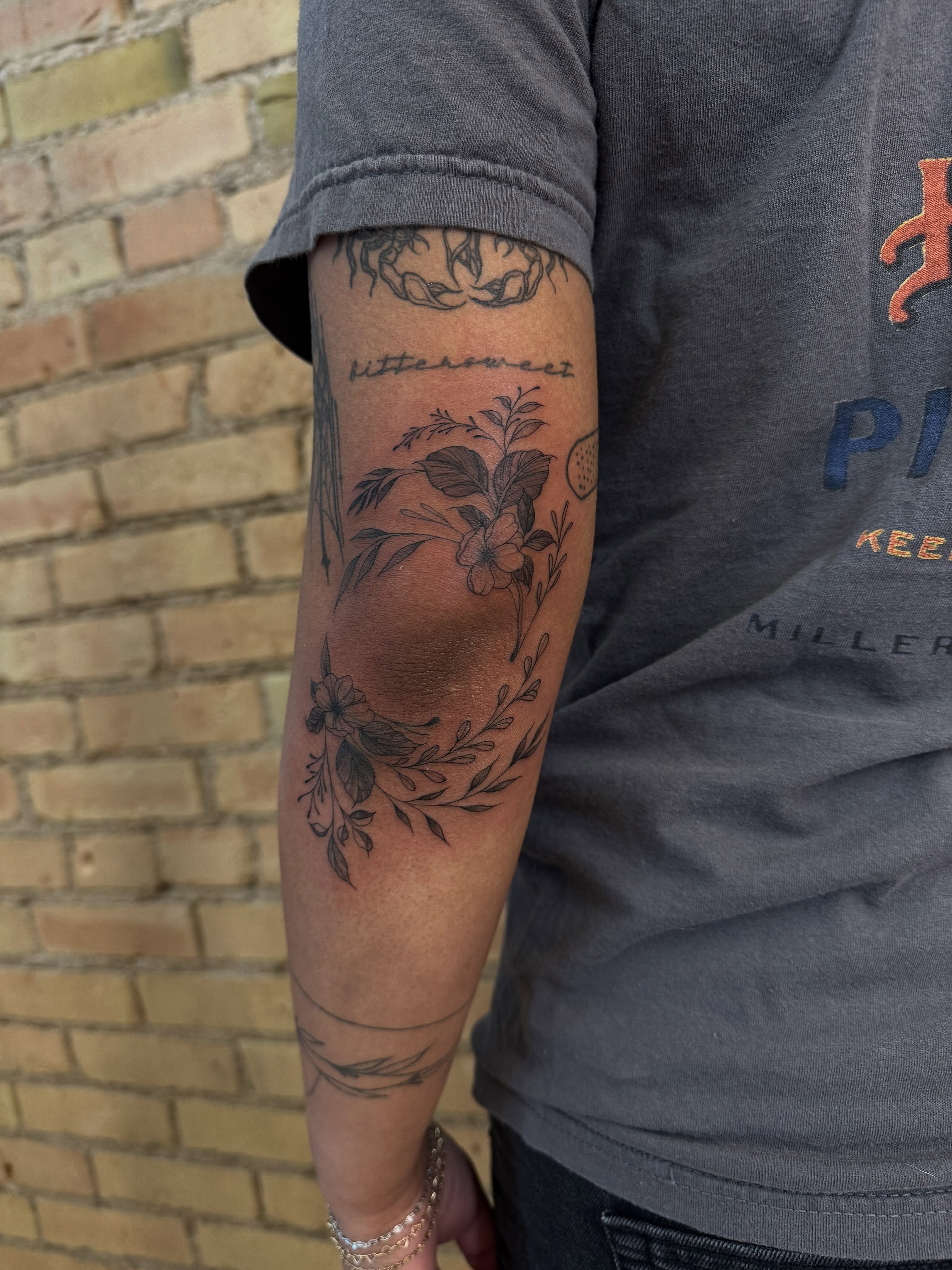 Botanical wreath black and grey tattoo on the forearm by Dre