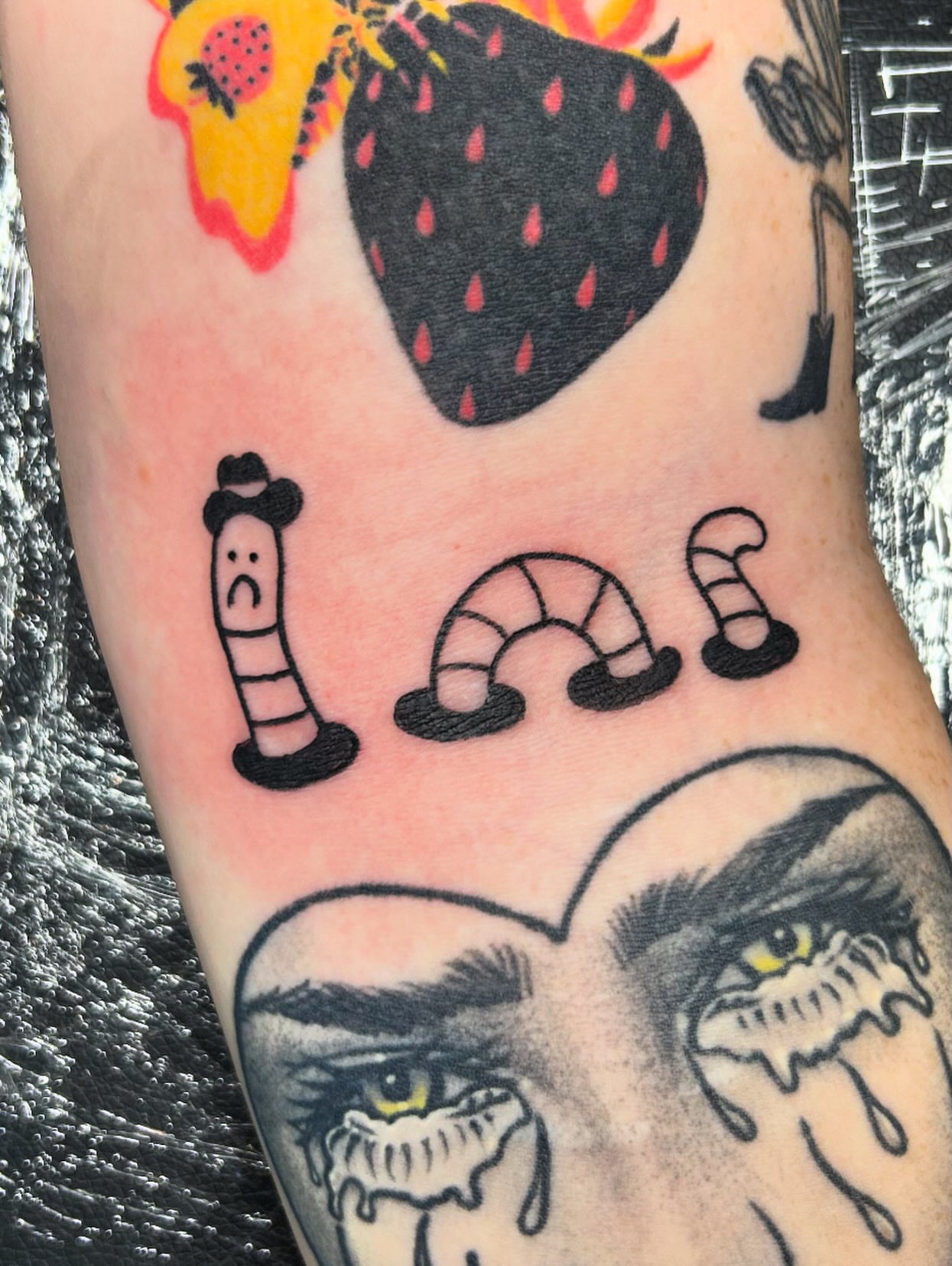 Strawberry and worm American traditional tattoo on the forearm by Nikki Power