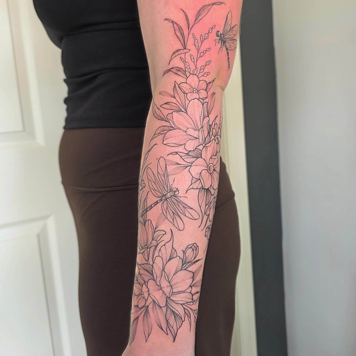 Flowers and dragonflies black and grey tattoo on the forearm by Dani Bond