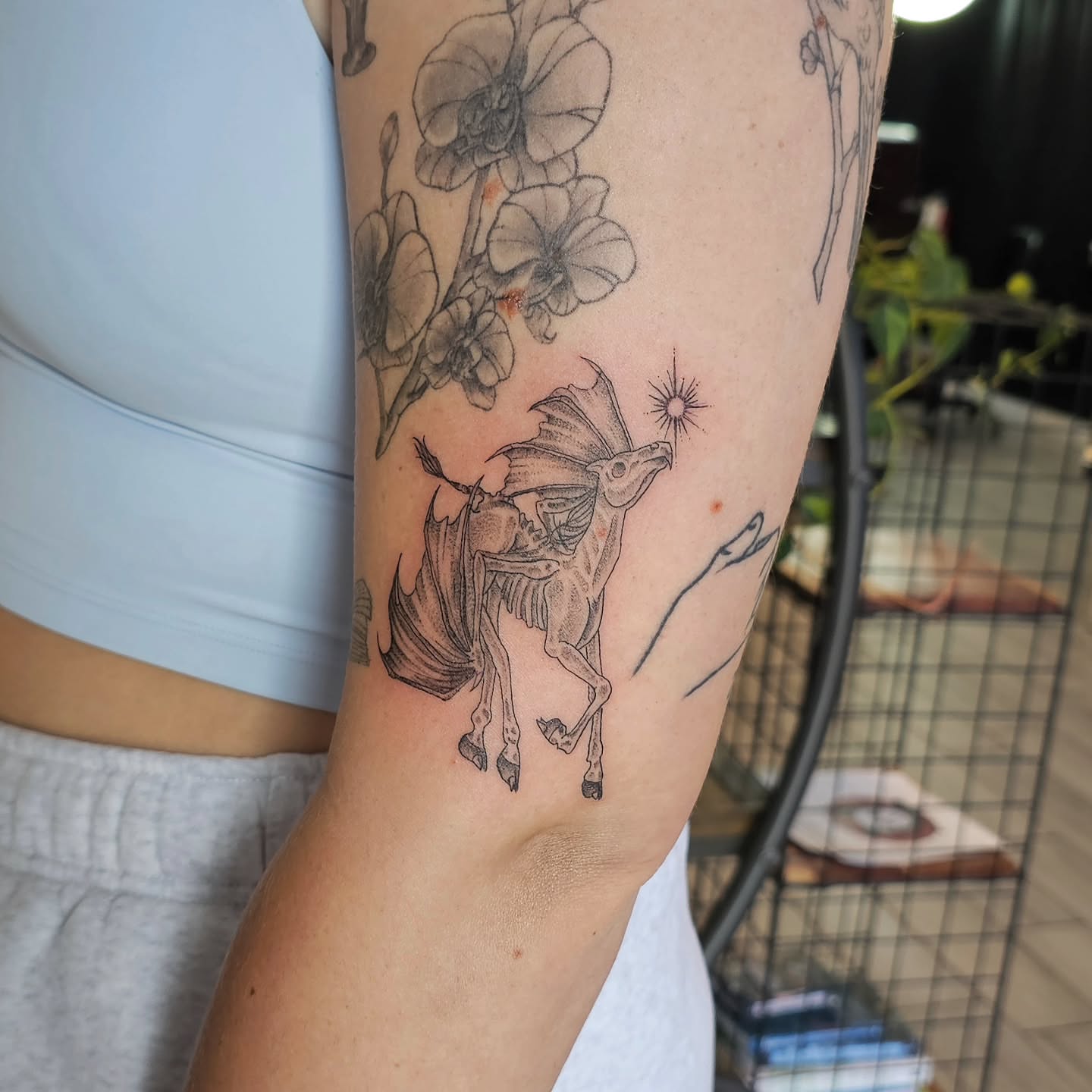 Mythical creature and flowers black and grey tattoo on the forearm by Casey Jo