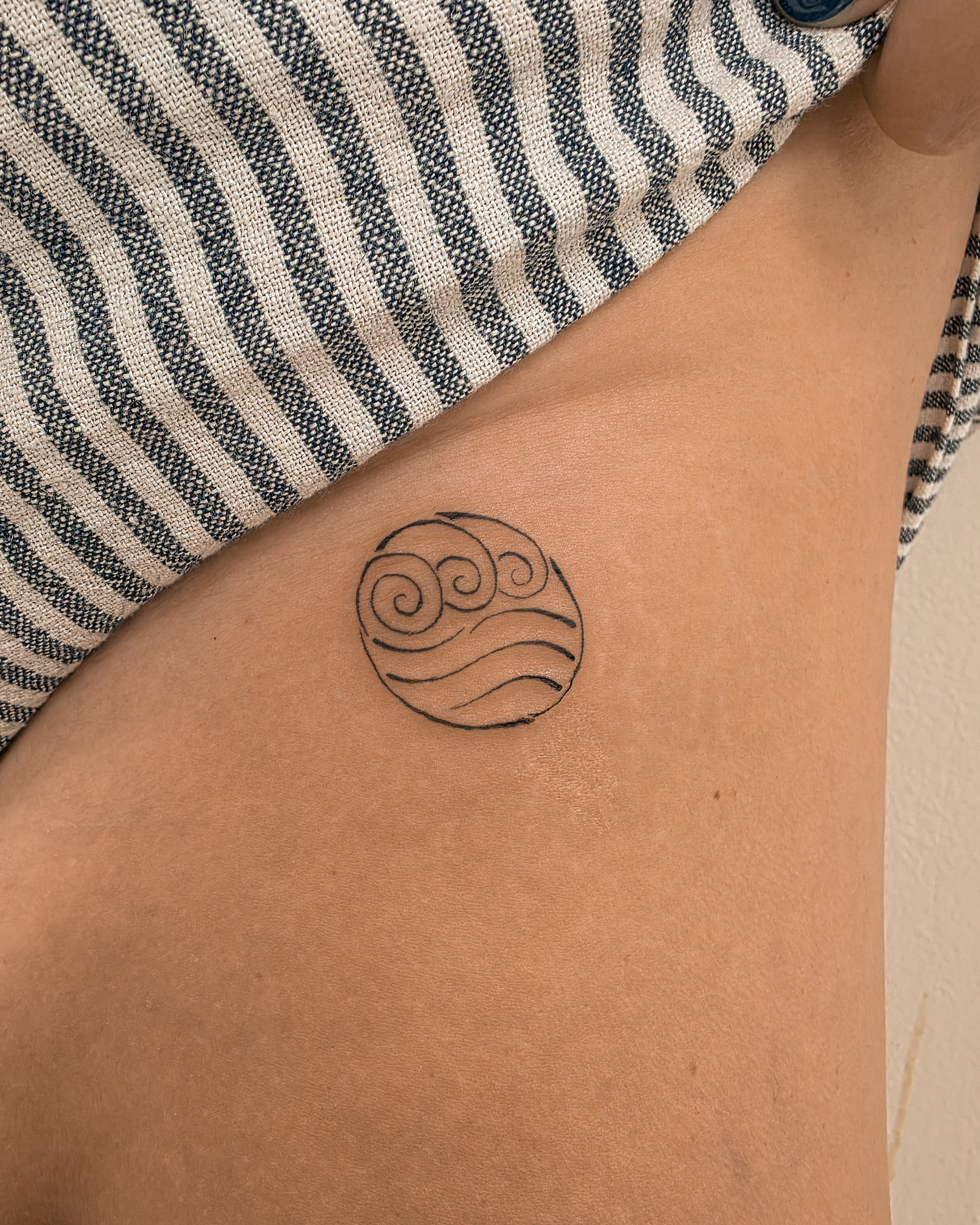 Water symbol minimalist tattoo on the thigh by Richmond tattoo shop, Richmond, Texas