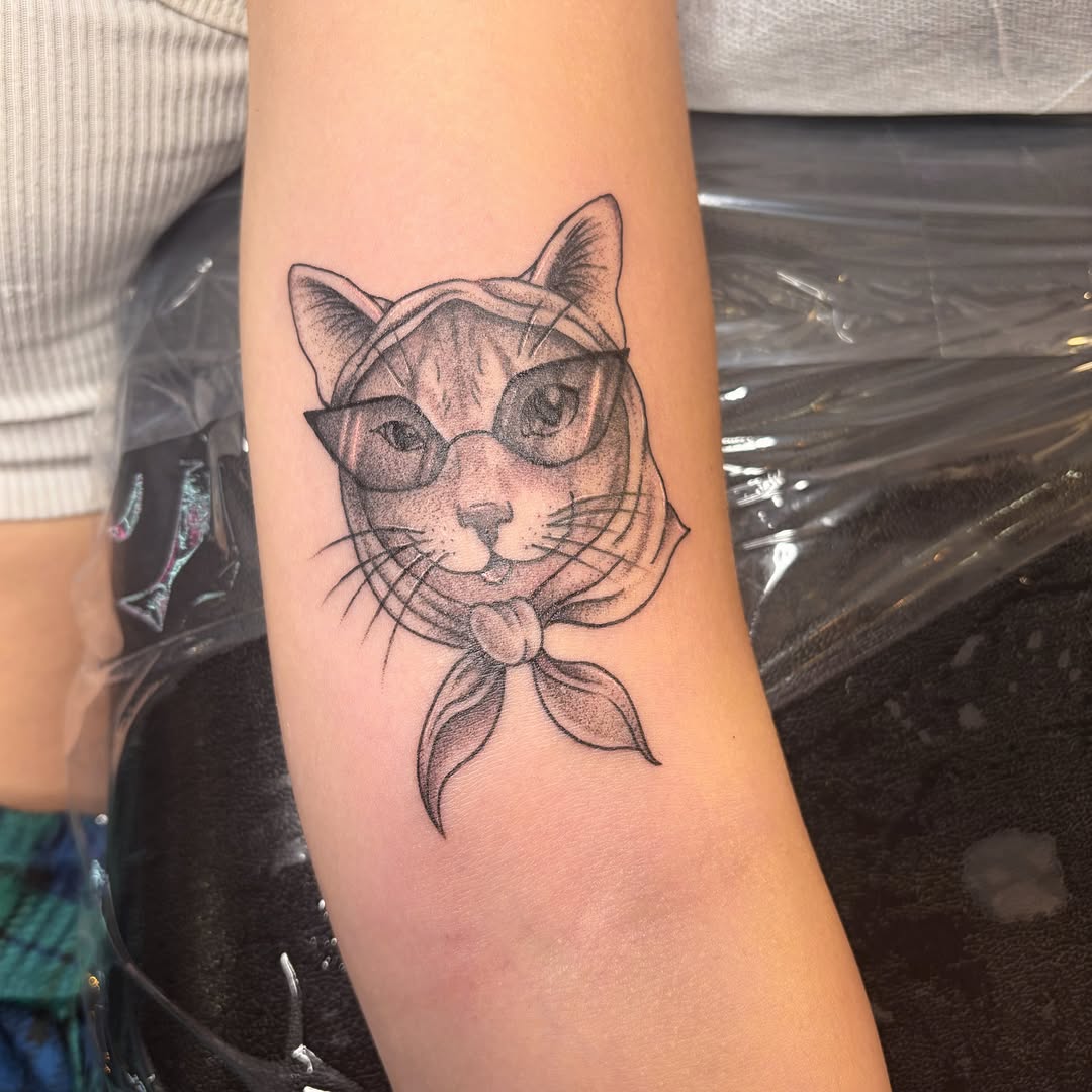 Cat wearing glasses and bandana dotwork tattoo on the forearm by Mary Hannah Sosdian