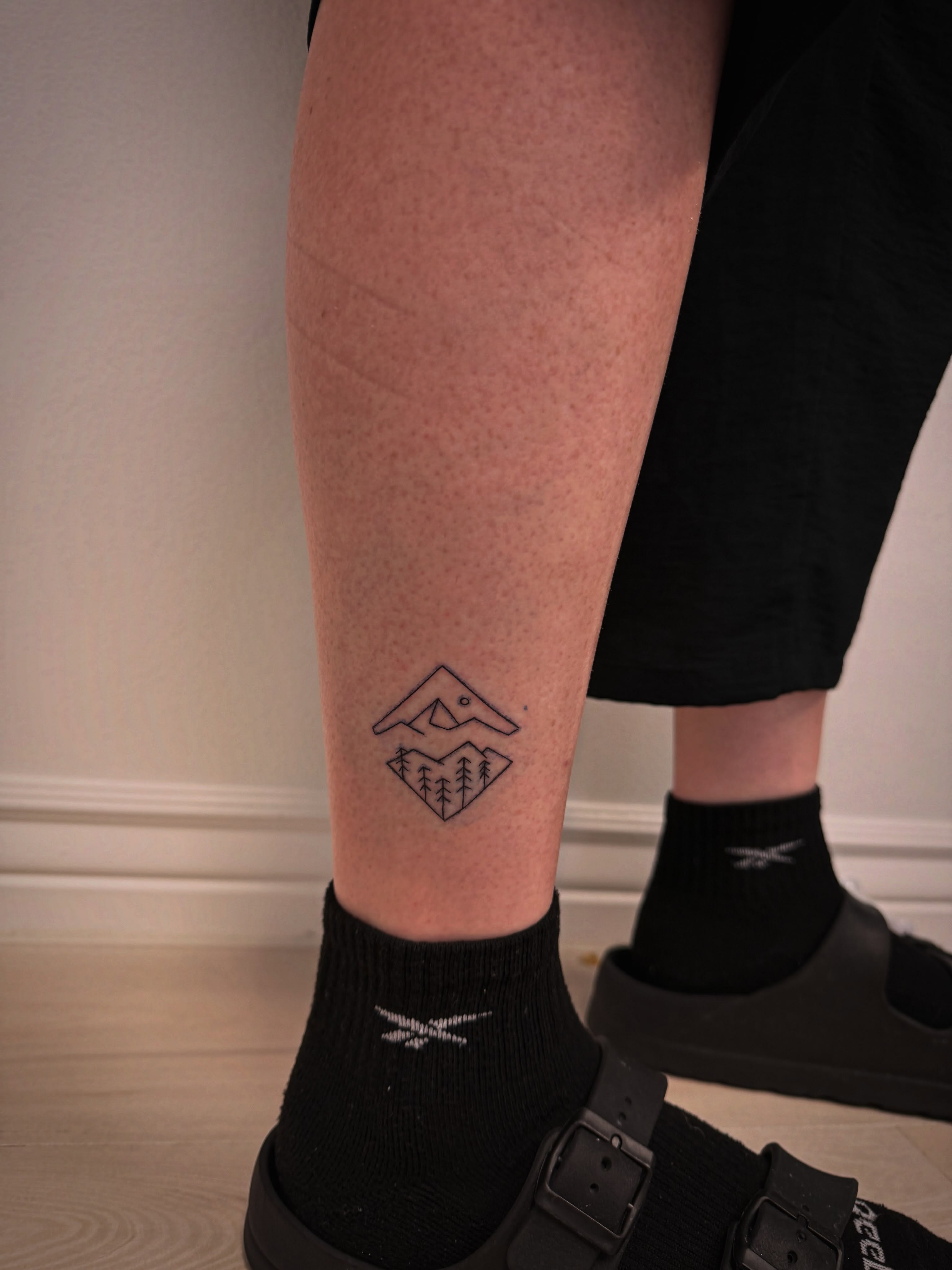 Mountain and trees geometric tattoo on the calf by Taylor Johnson