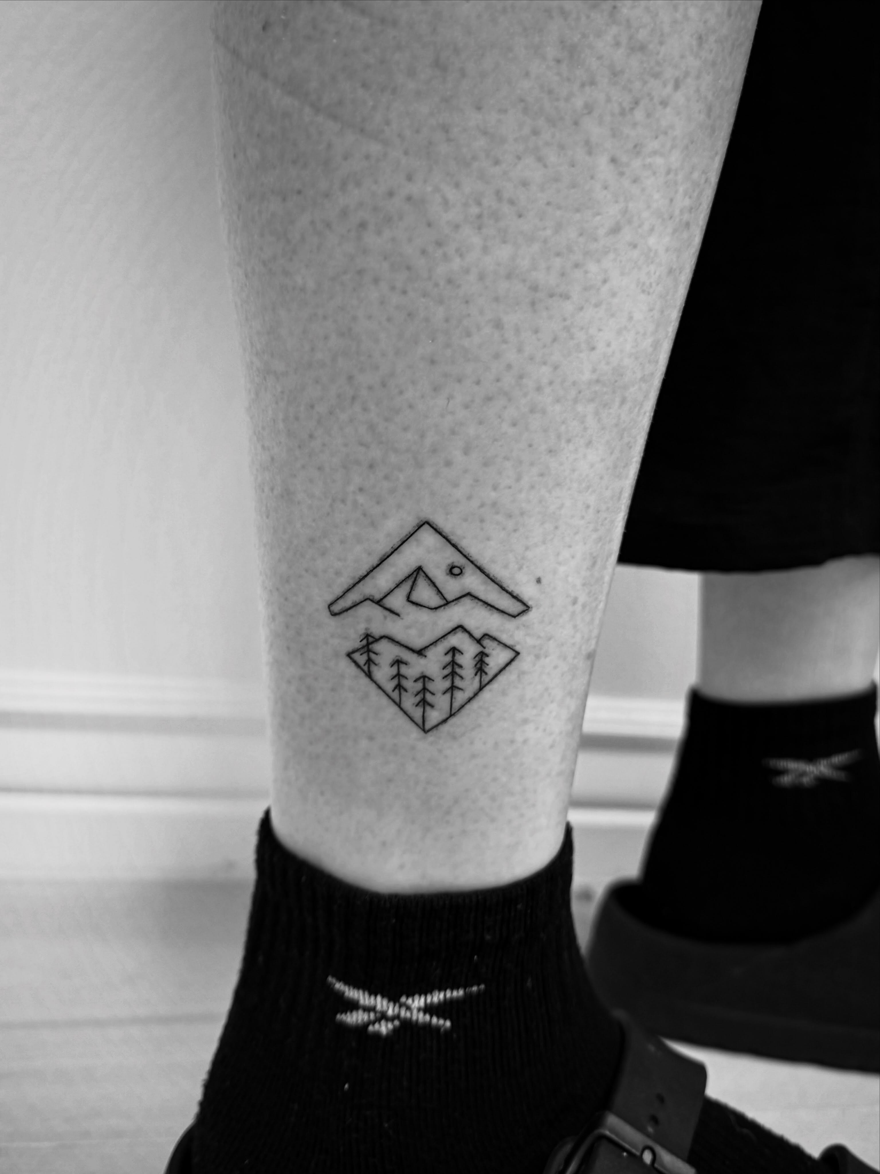 Mountain and trees geometric tattoo on the calf by Taylor Johnson
