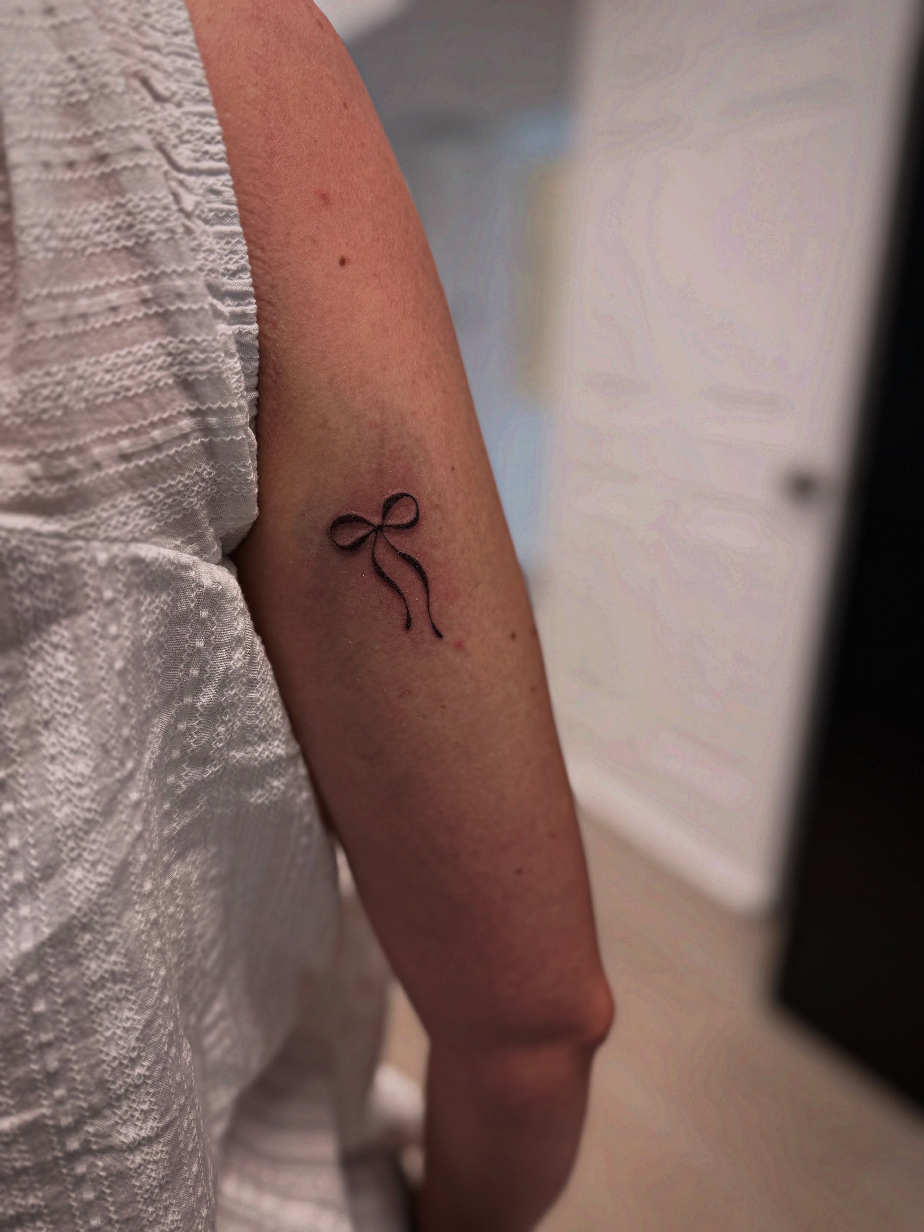 Bow minimalist tattoo on the forearm by Taylor Johnson