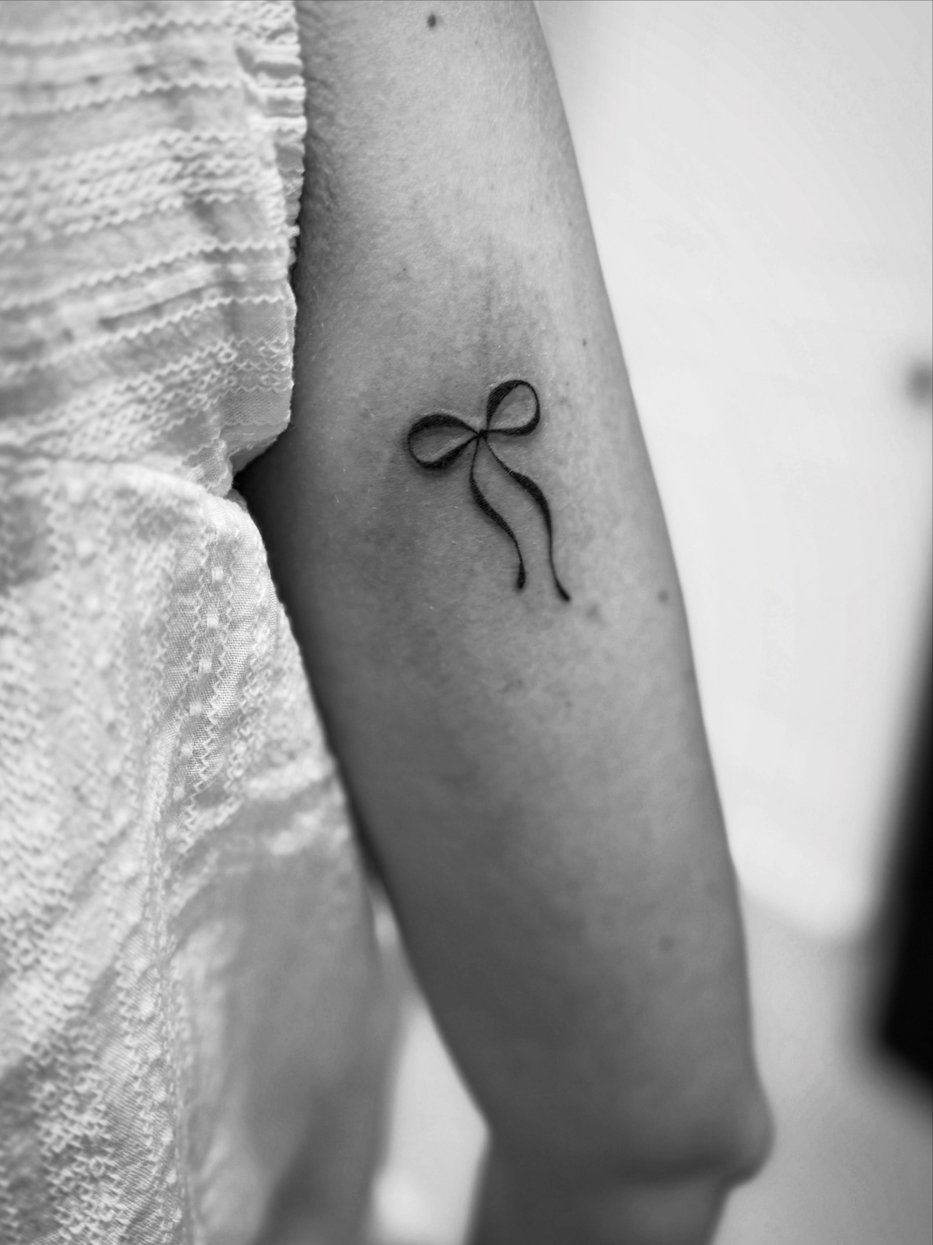 Bow fine line tattoo on the forearm by Taylor Johnson