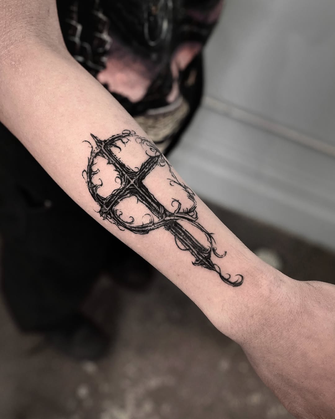 Cross with thorns black and grey tattoo on the forearm by Gun