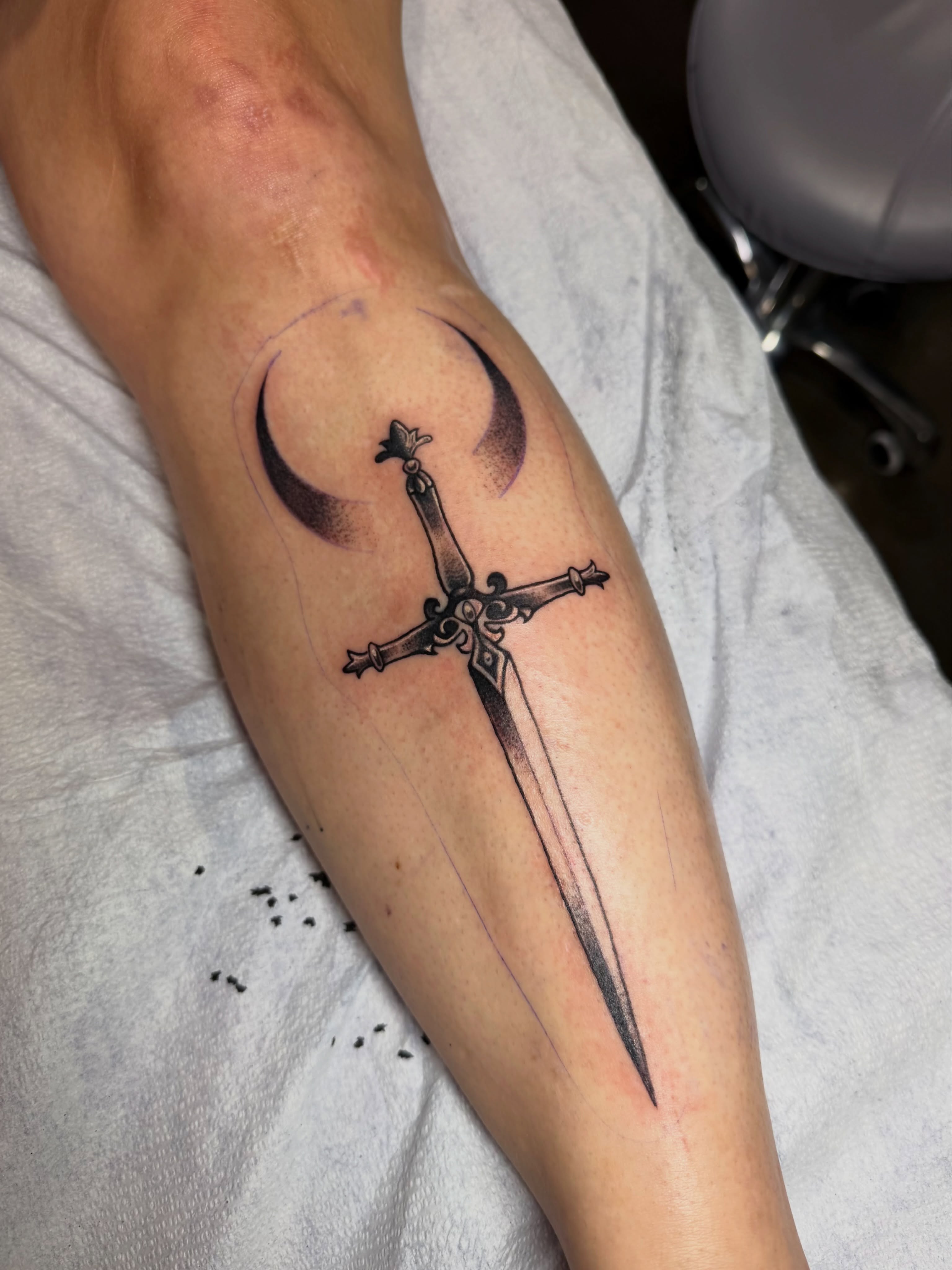 Sword and crescent moon black and grey tattoo on the forearm by Emmie Turner