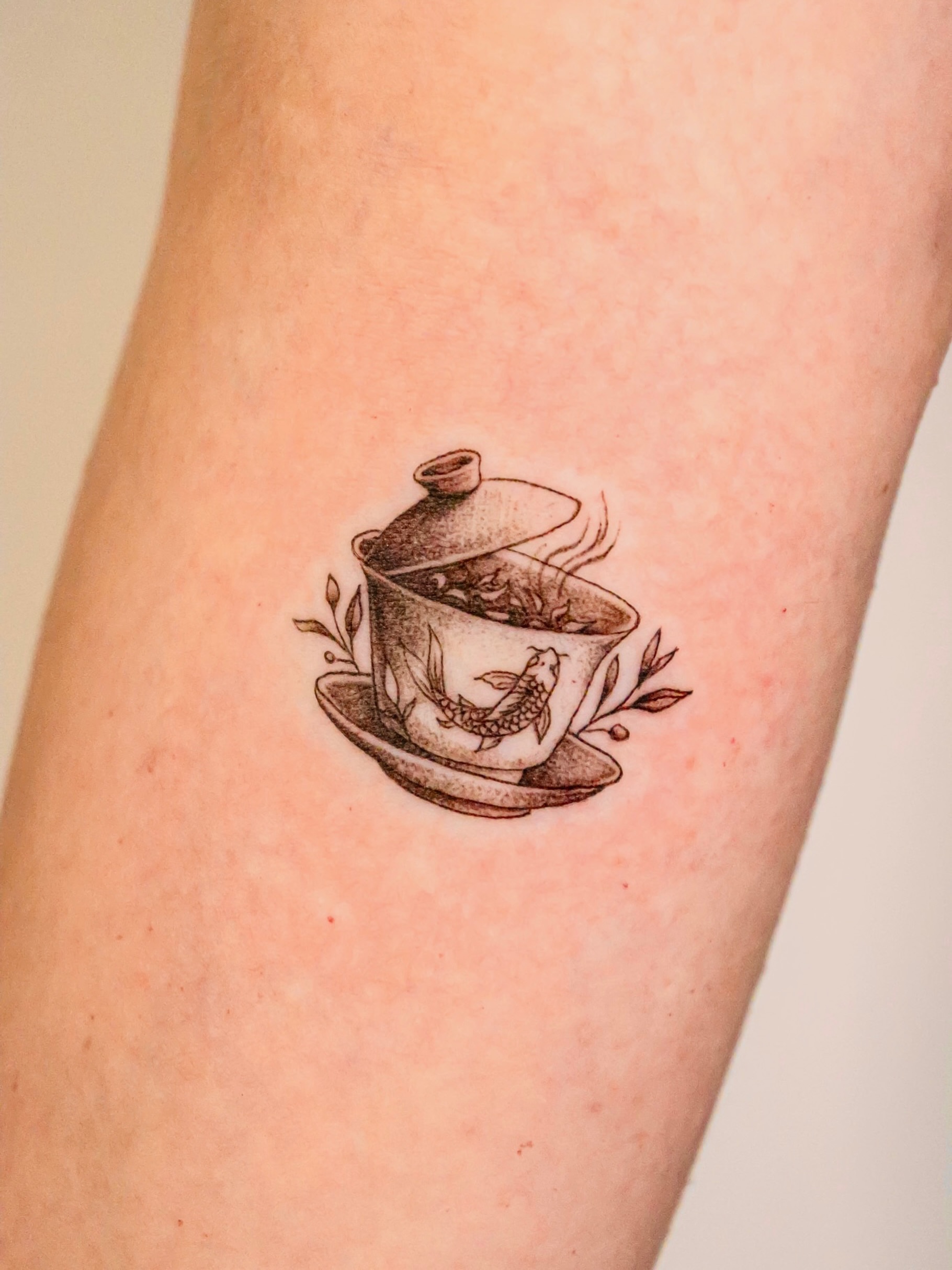 Teapot and fish black and grey tattoo on the forearm by Angel Tattoos