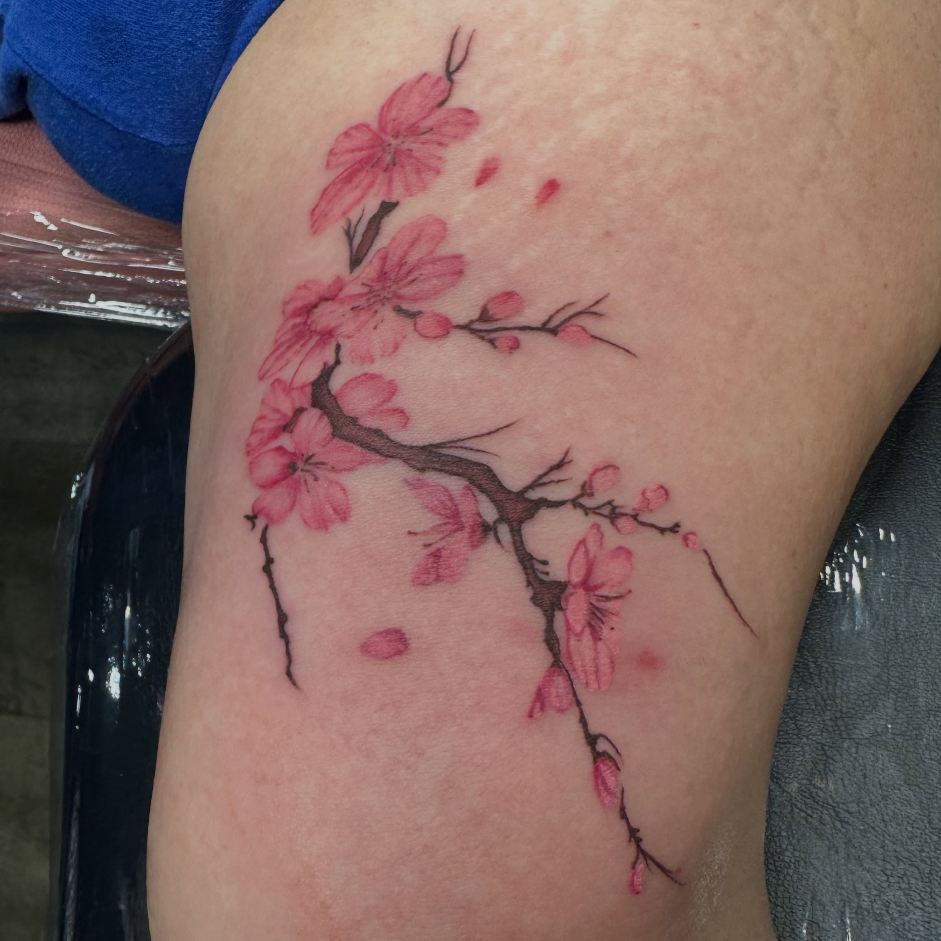 Cherry blossom branch watercolor tattoo on the thigh by Svetlana