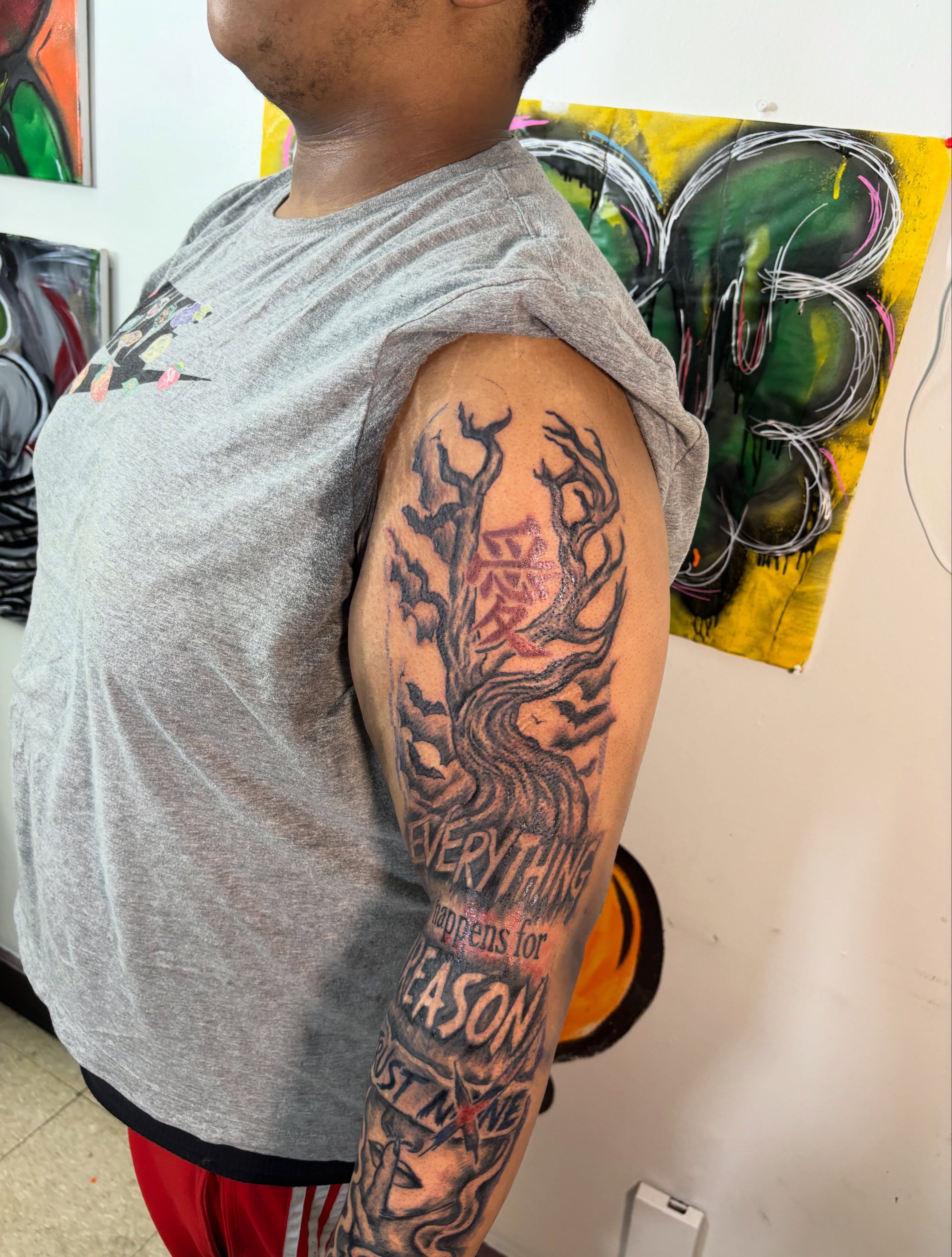 Tree with Japanese characters black and grey tattoo on the upper arm by Exotic Motion🌪️