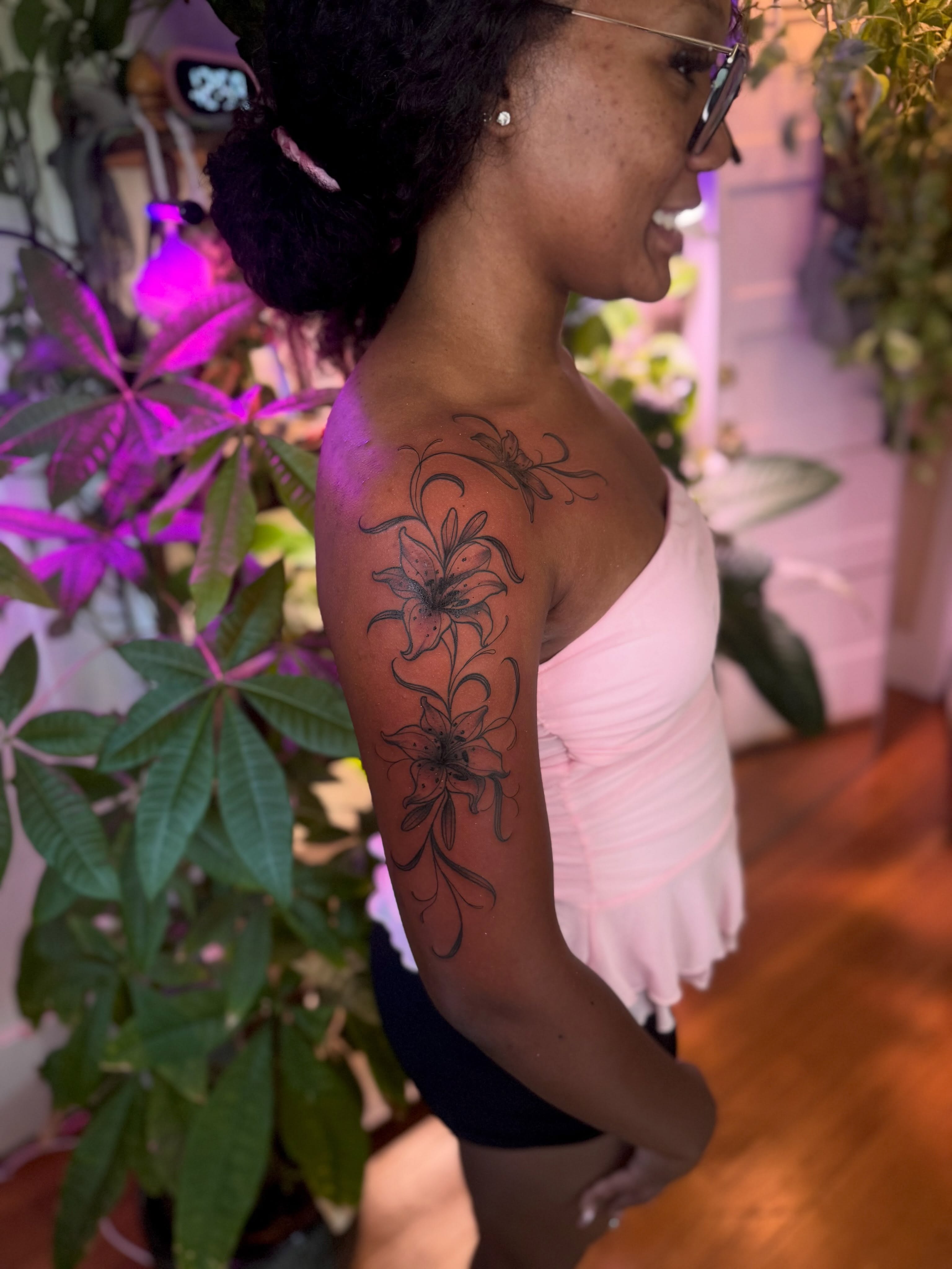 Lilies black and grey tattoo on the upper arm by Angie Cotton