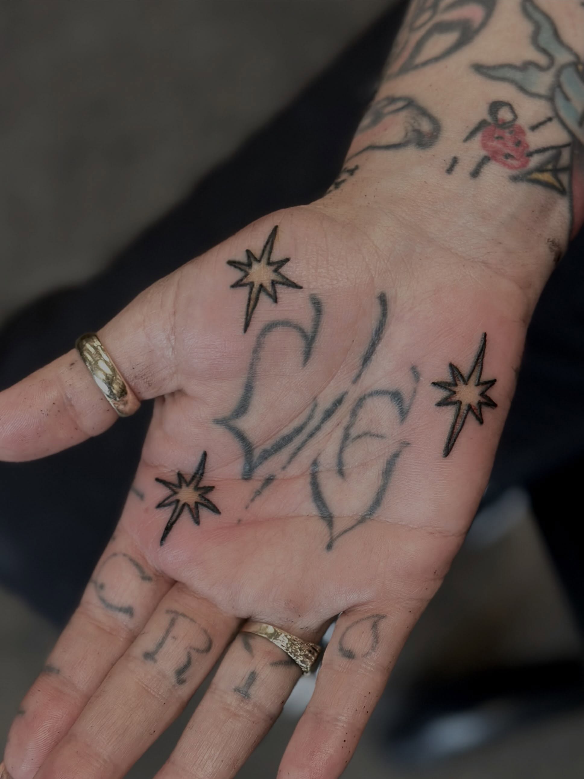 Stars and cursive black and grey tattoo on the hand by Kat Fishbein
