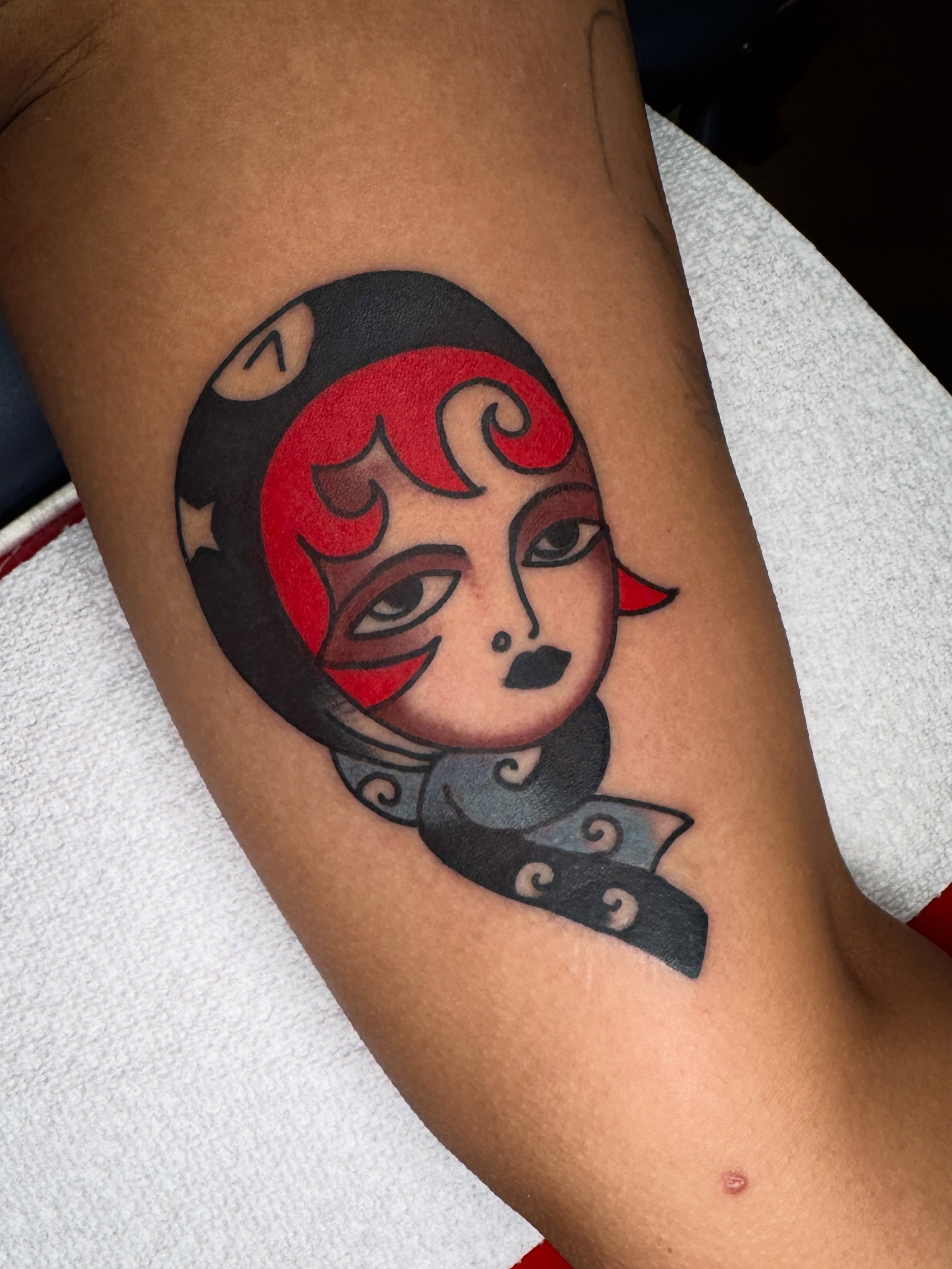 Mask-like figure American traditional tattoo on the forearm by lily gustave i tattoo