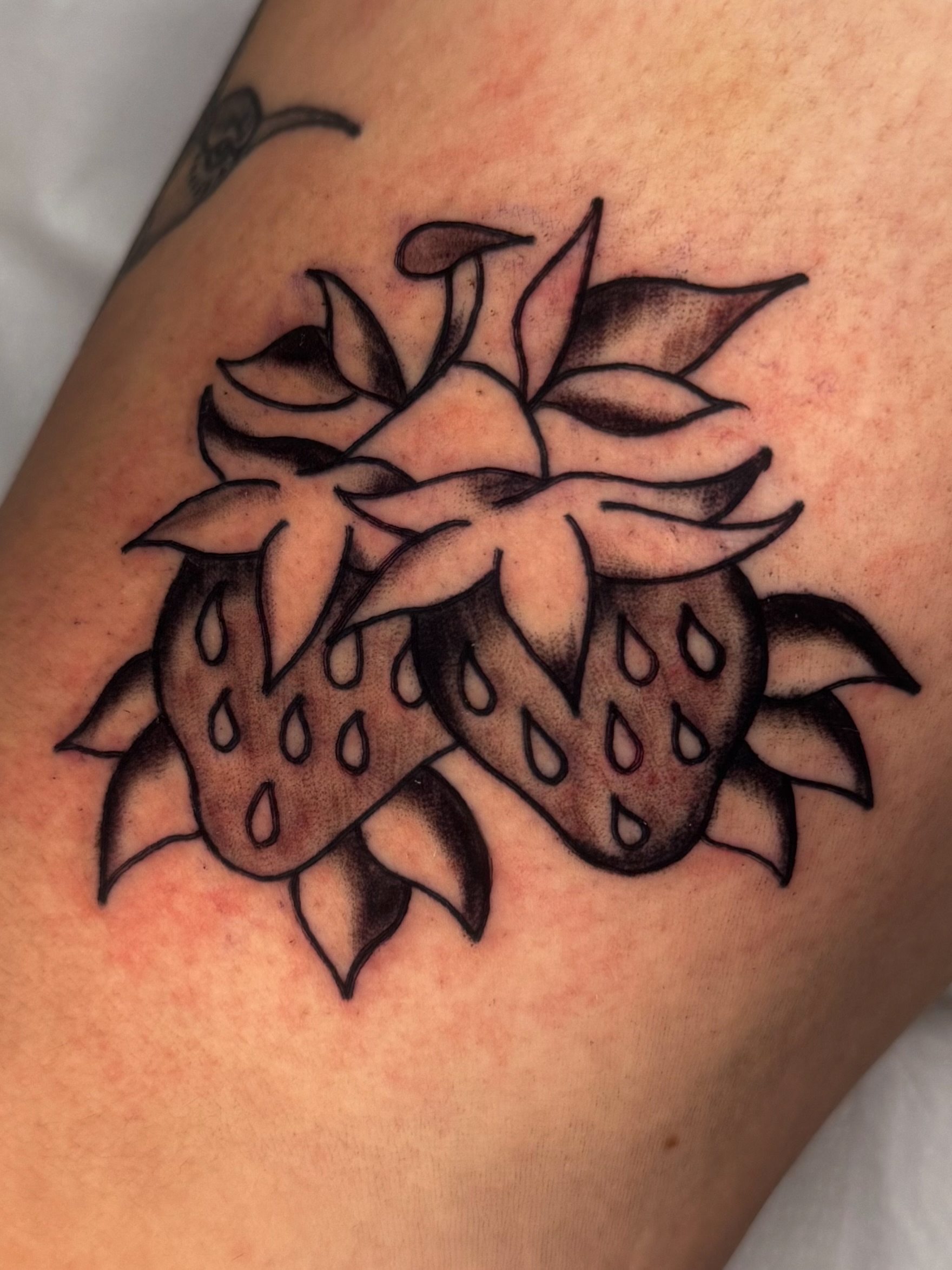 Strawberries black and grey tattoo on the upper arm by Lexie Graff