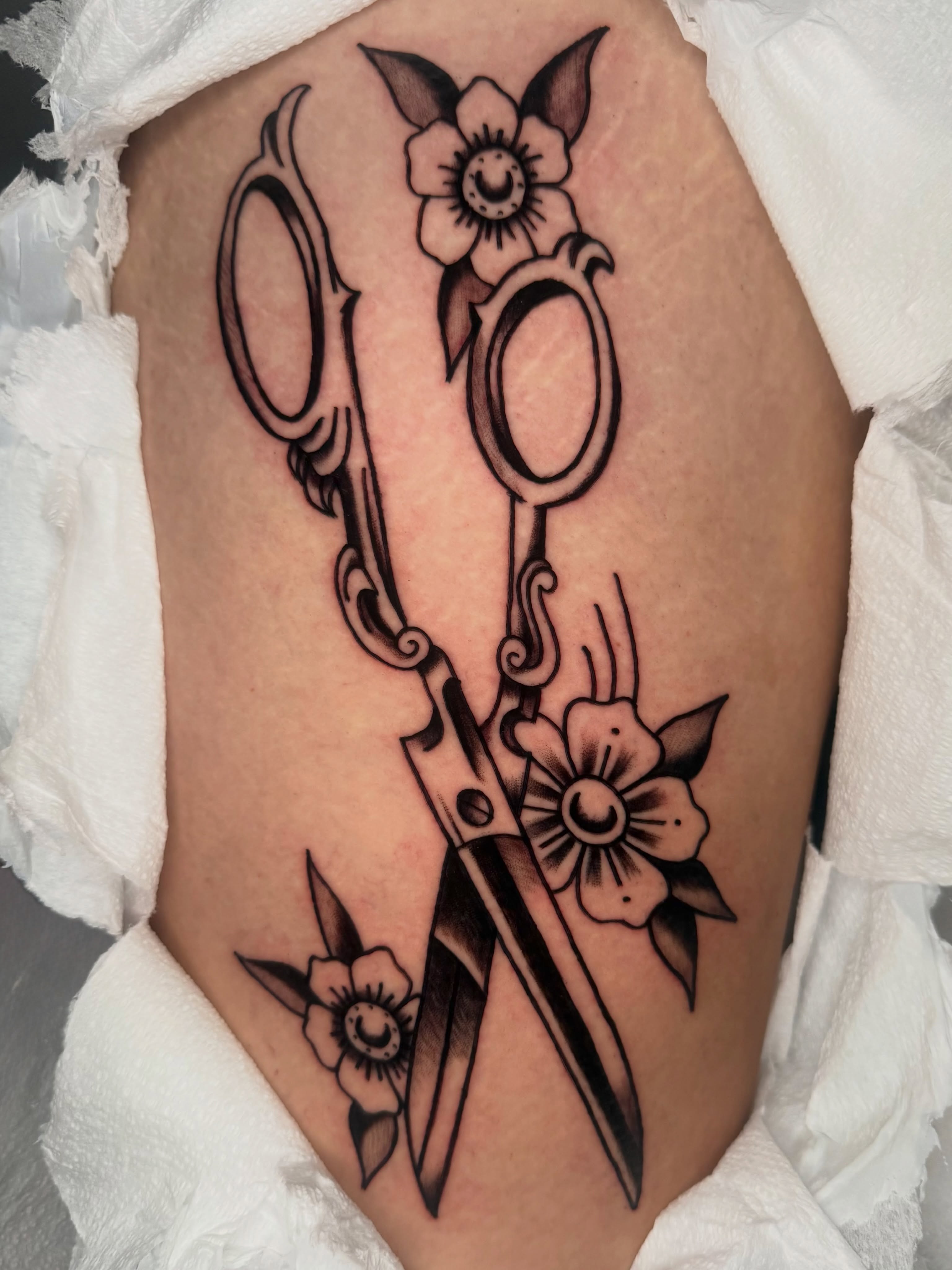 Scissors and flowers black and grey tattoo on the thigh by Lexie Graff