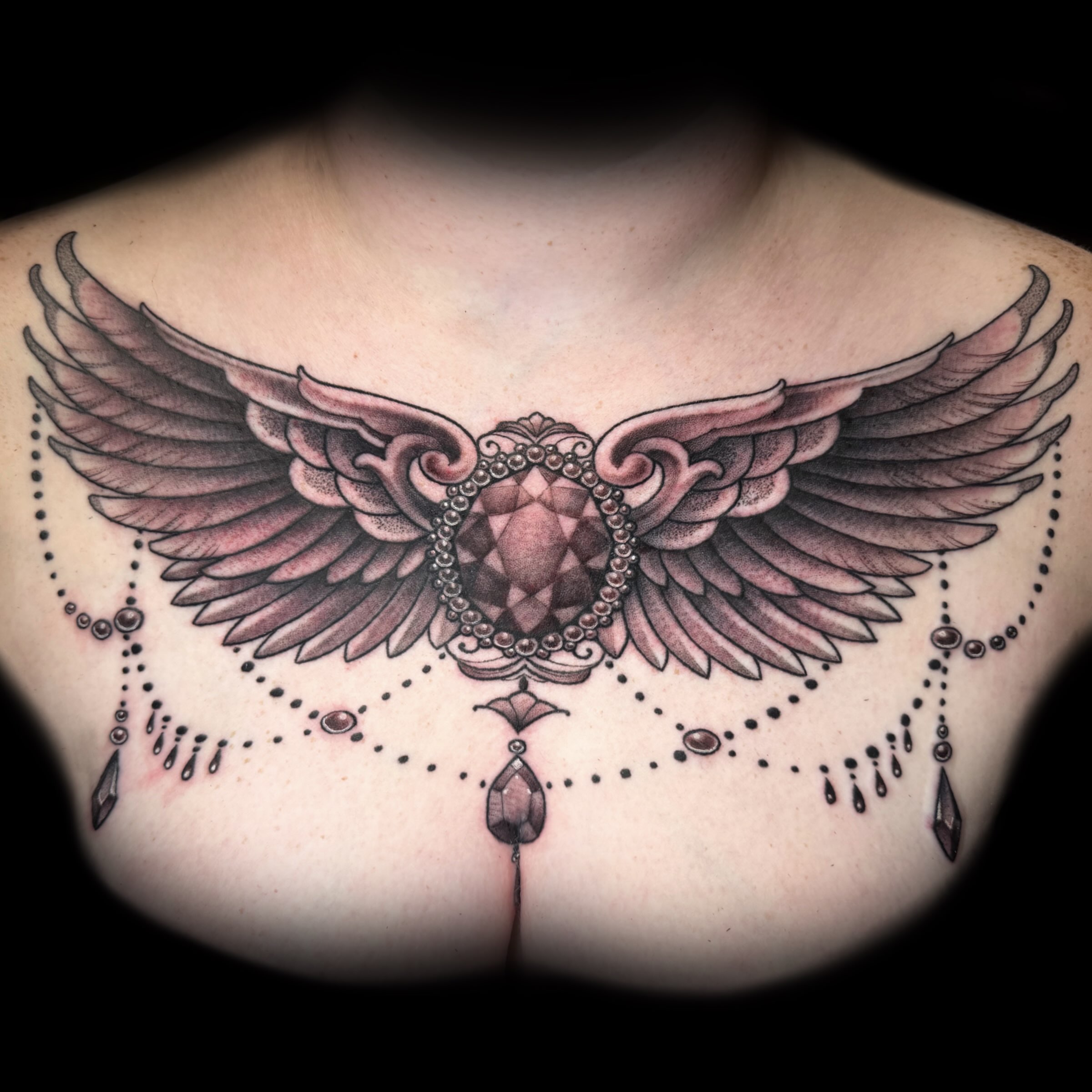 Wings and gem geometric tattoo on the chest by Kelsea Weir McCree