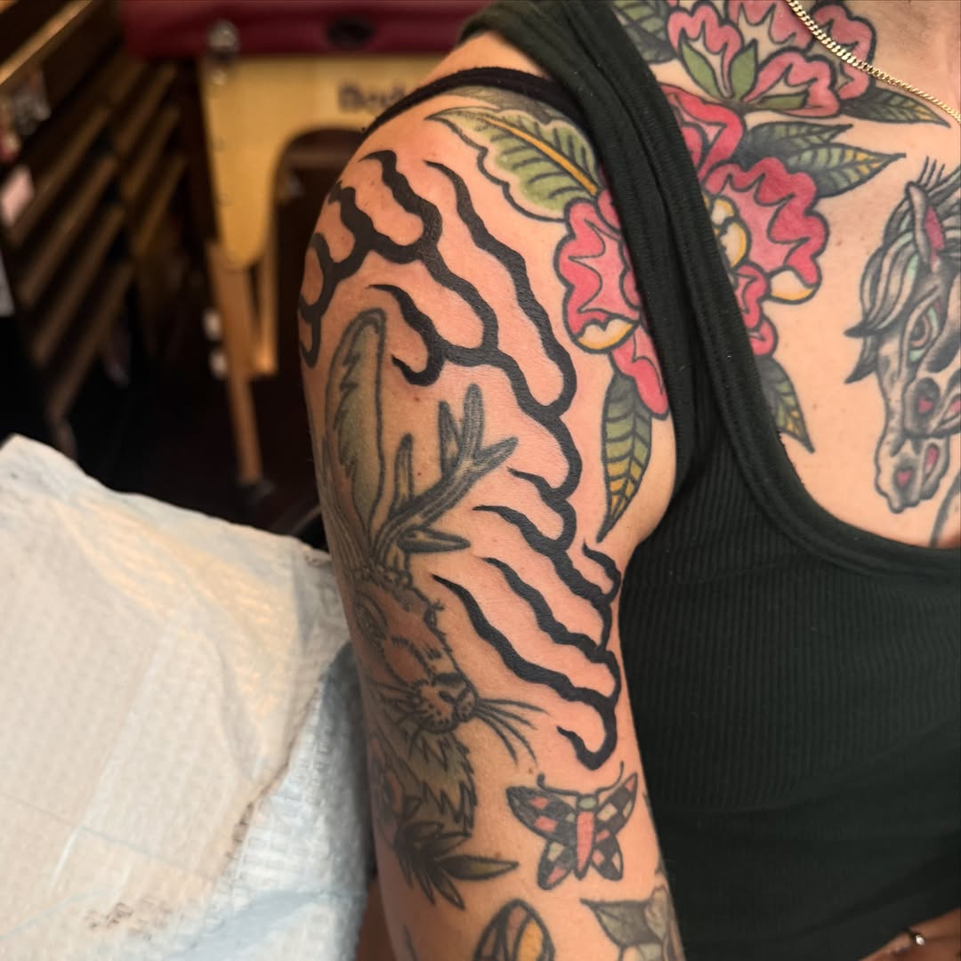 Tiger stripes and flowers American traditional tattoo on the upper arm by Julia Louise