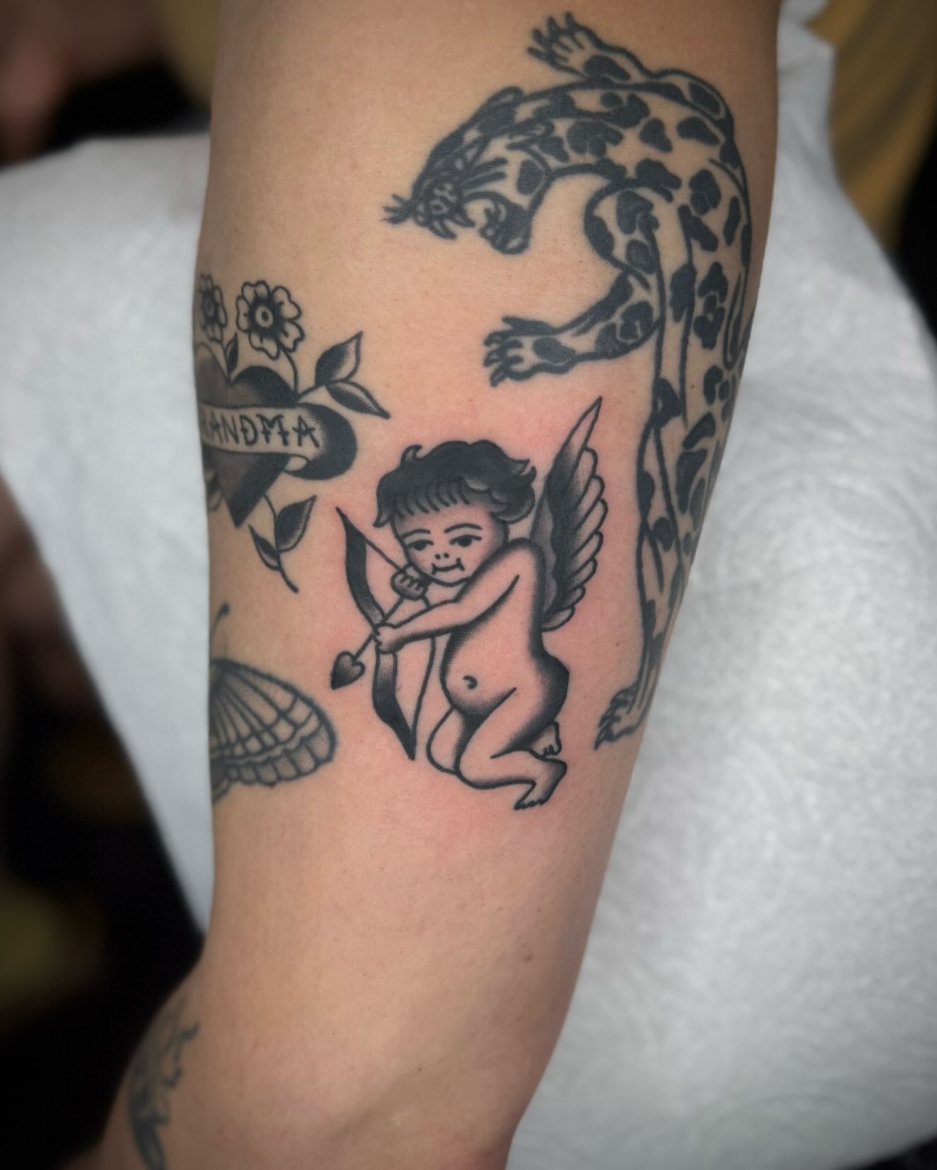 Cherub with bow black and grey tattoo on the forearm by kalli berry