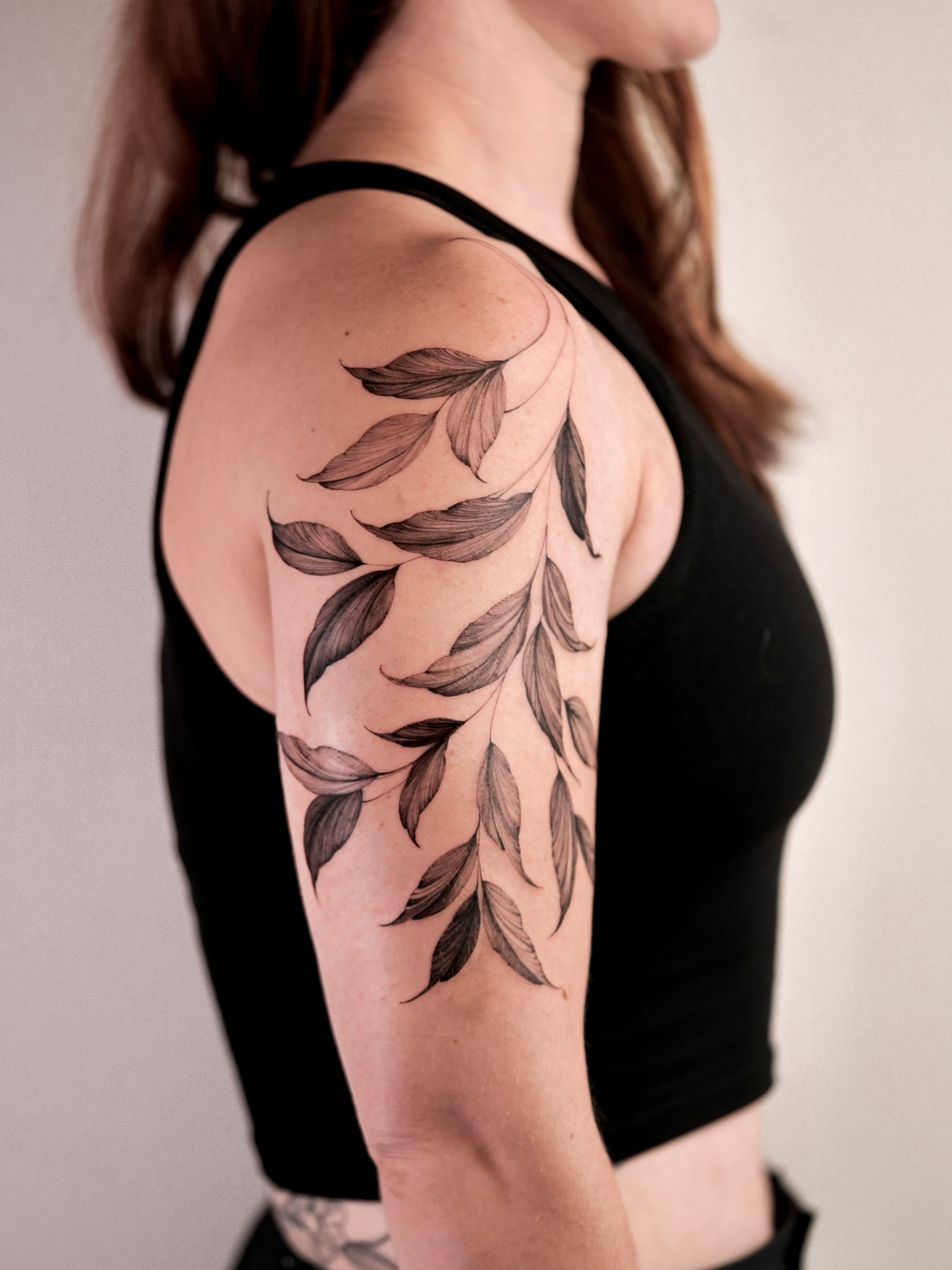 Leaf branch black and grey tattoo on the upper arm by Zalina Loriia