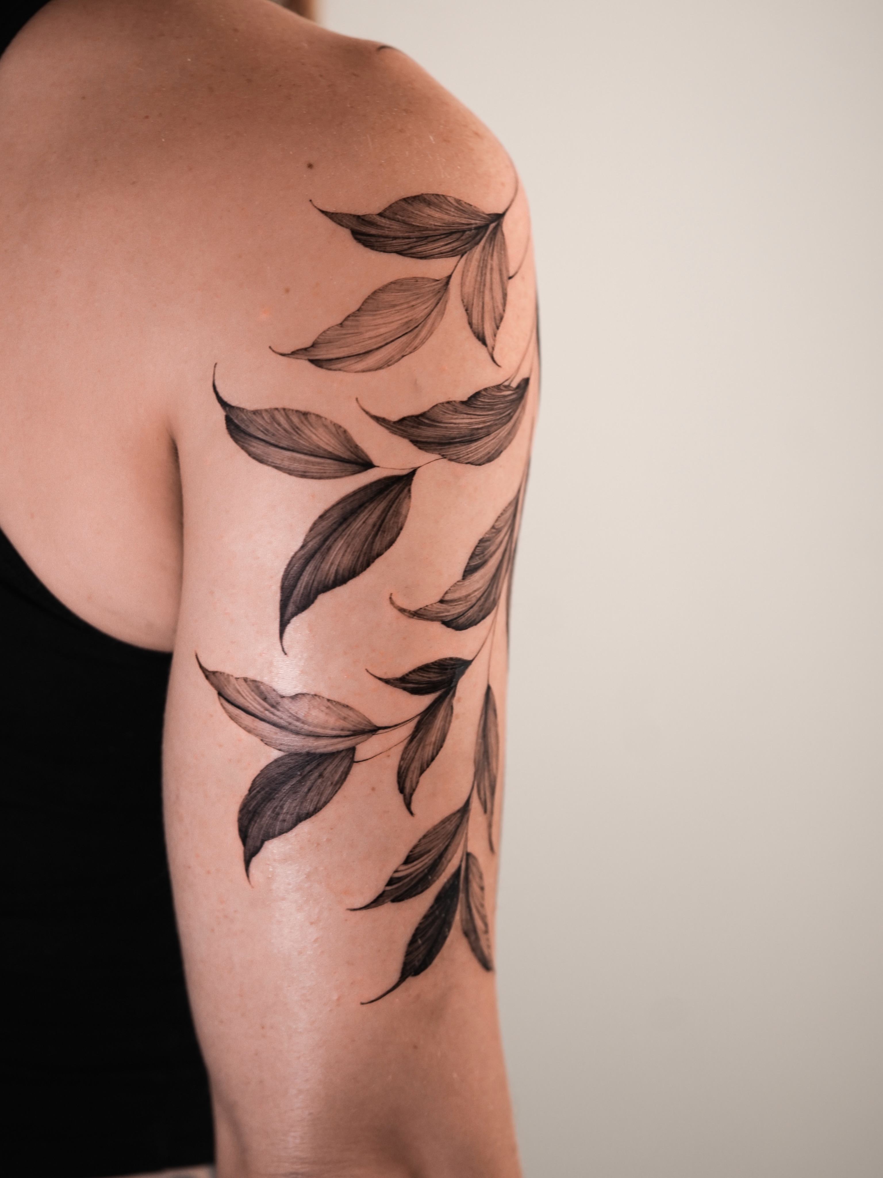 Leaf branch black and grey tattoo on the upper arm by Zalina Loriia