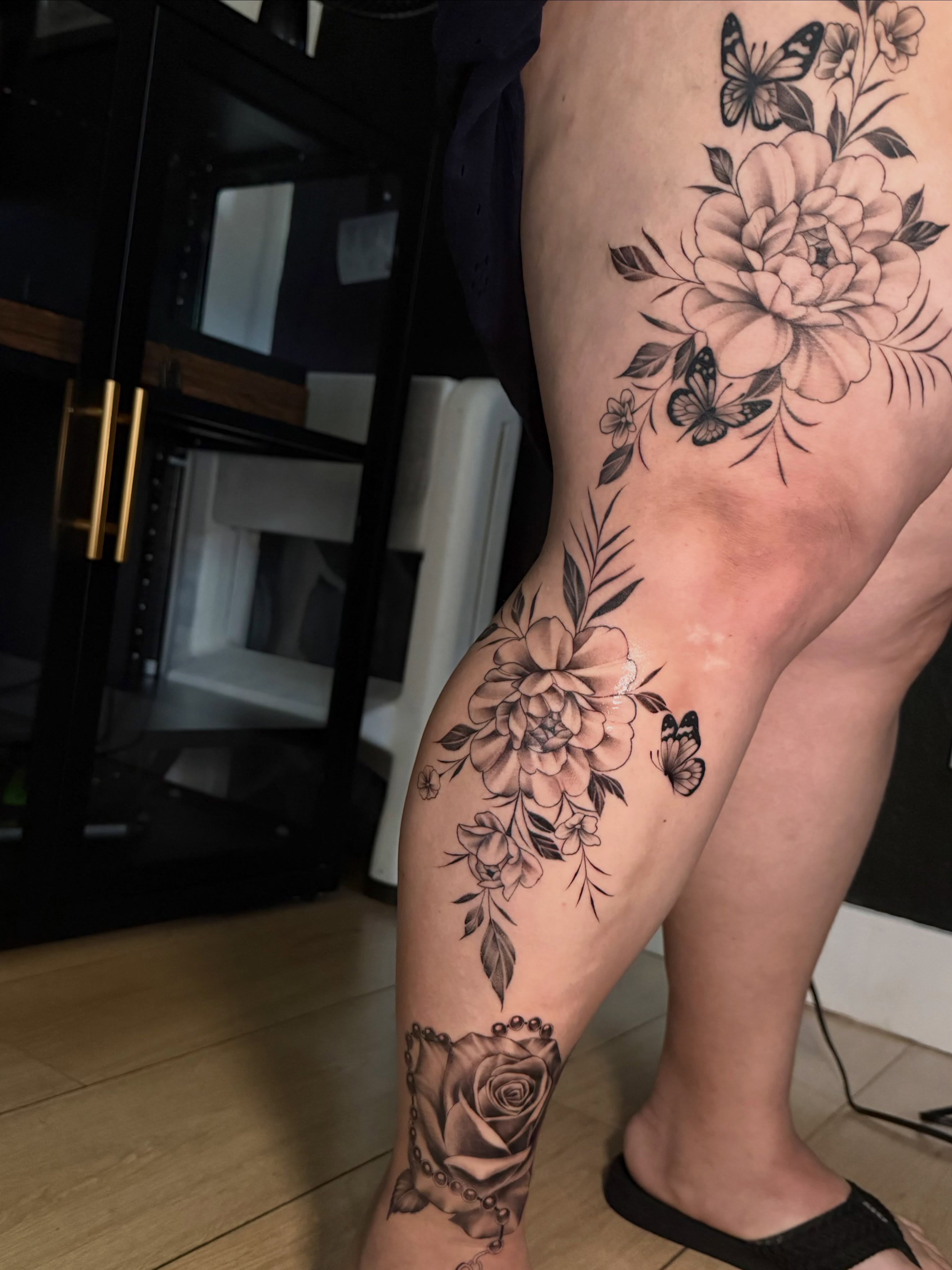 Floral bouquet black and grey tattoo on the thigh by Faith Lopez