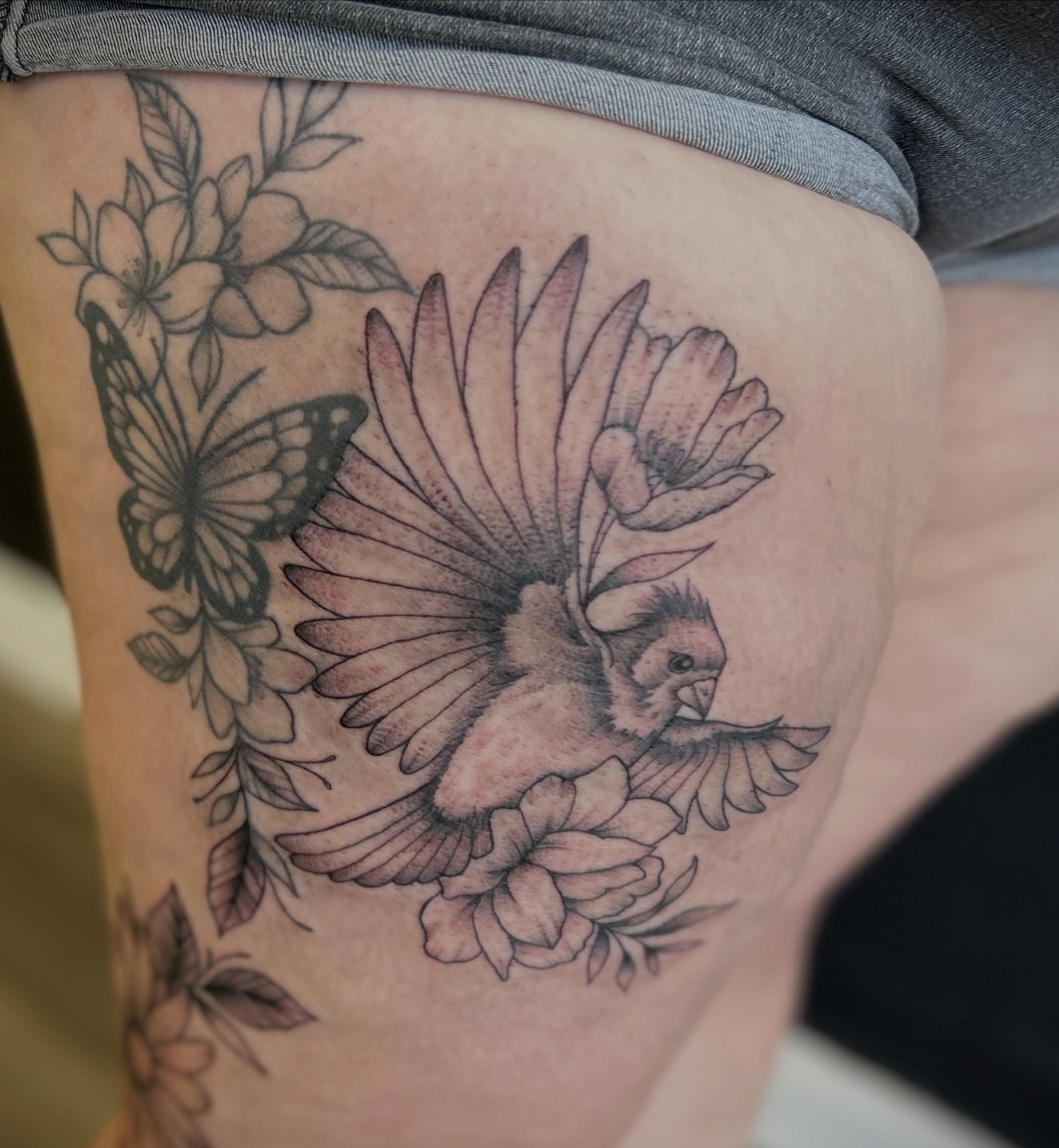 Bird and flowers black and grey tattoo on the thigh by Browtique & Ink, Clearwater, Florida