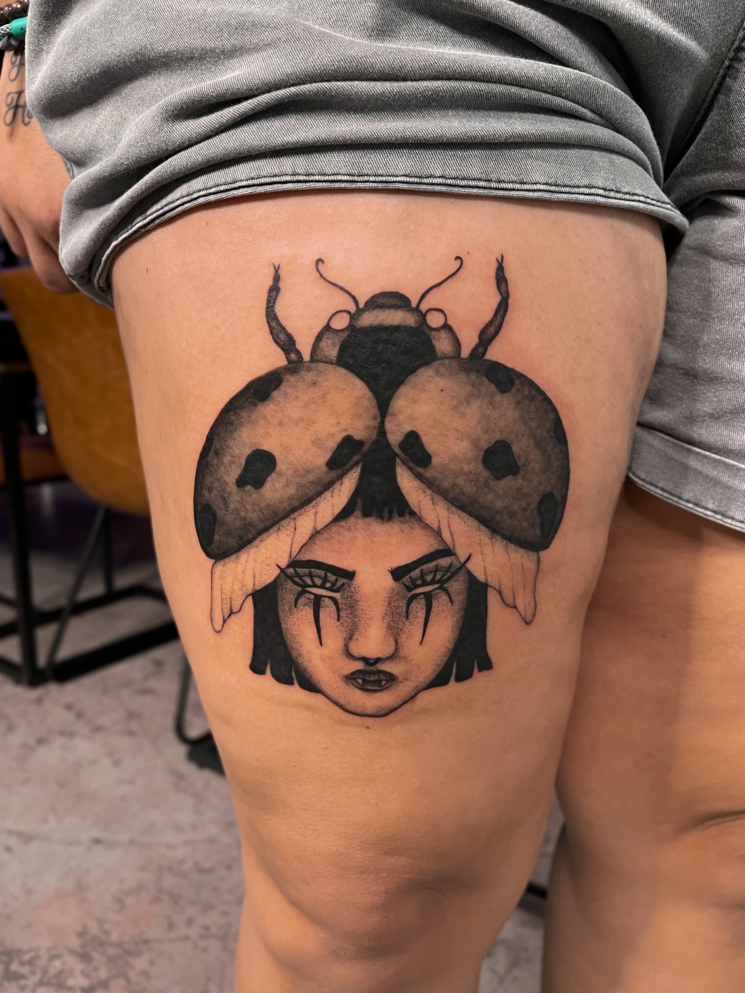 Ladybug black and grey tattoo on the thigh by Amy