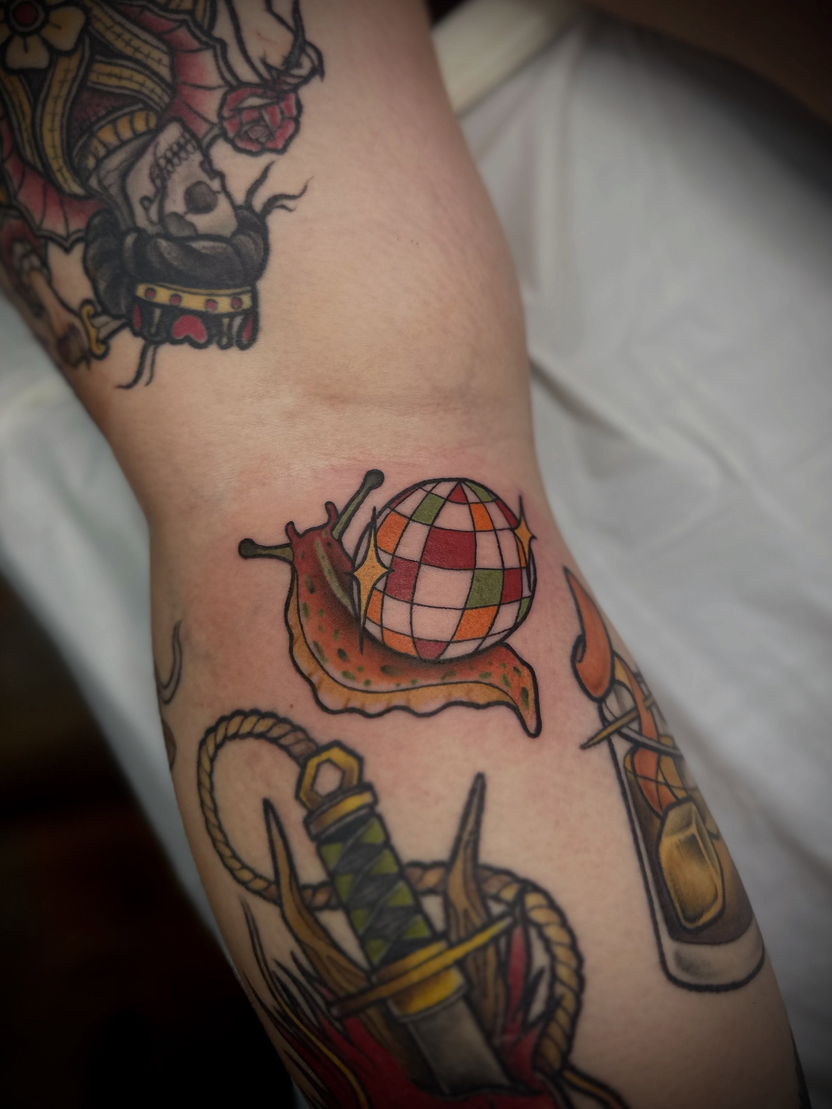 Snail with checkered shell American traditional tattoo on the forearm by Madison Orchard Tattoos