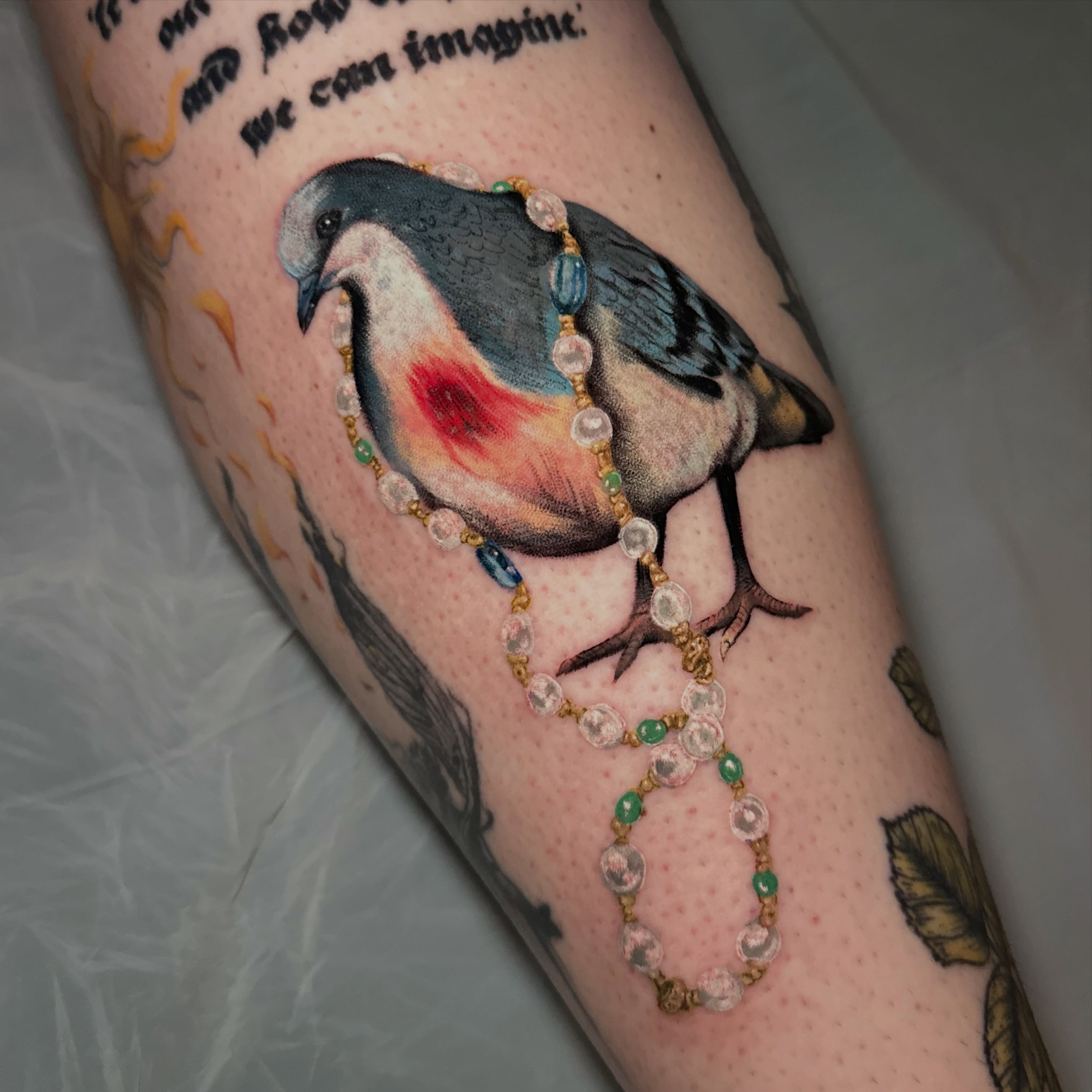 Bird with rosary realism tattoo on the forearm by Les
