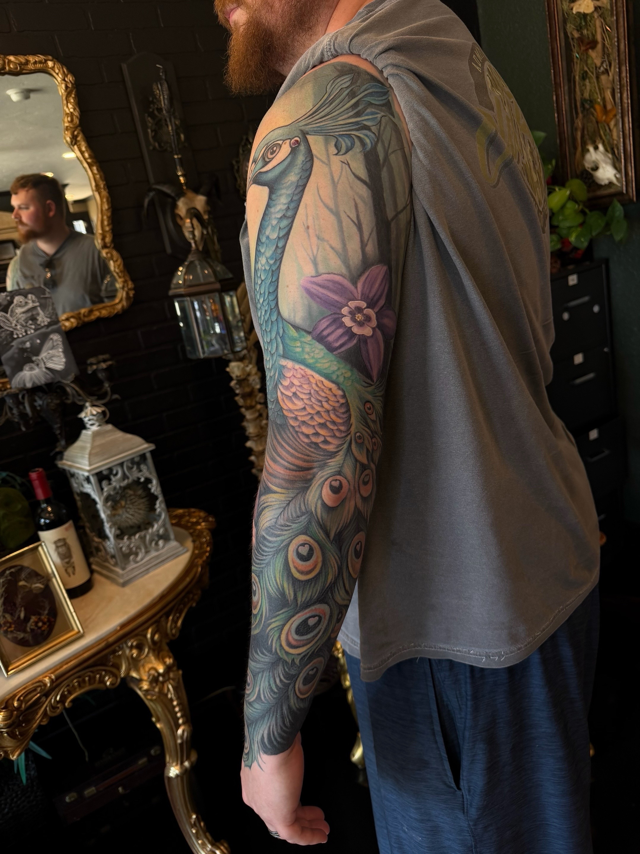 Peacock and floral realism tattoo on the upper arm by Shae Sullivan