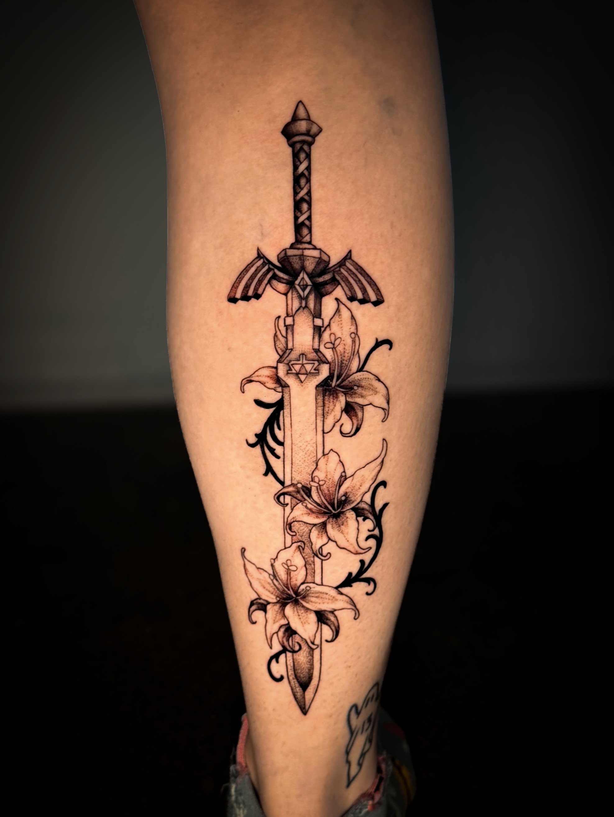 Sword and lilies ornamental tattoo on the forearm by Kam Mills