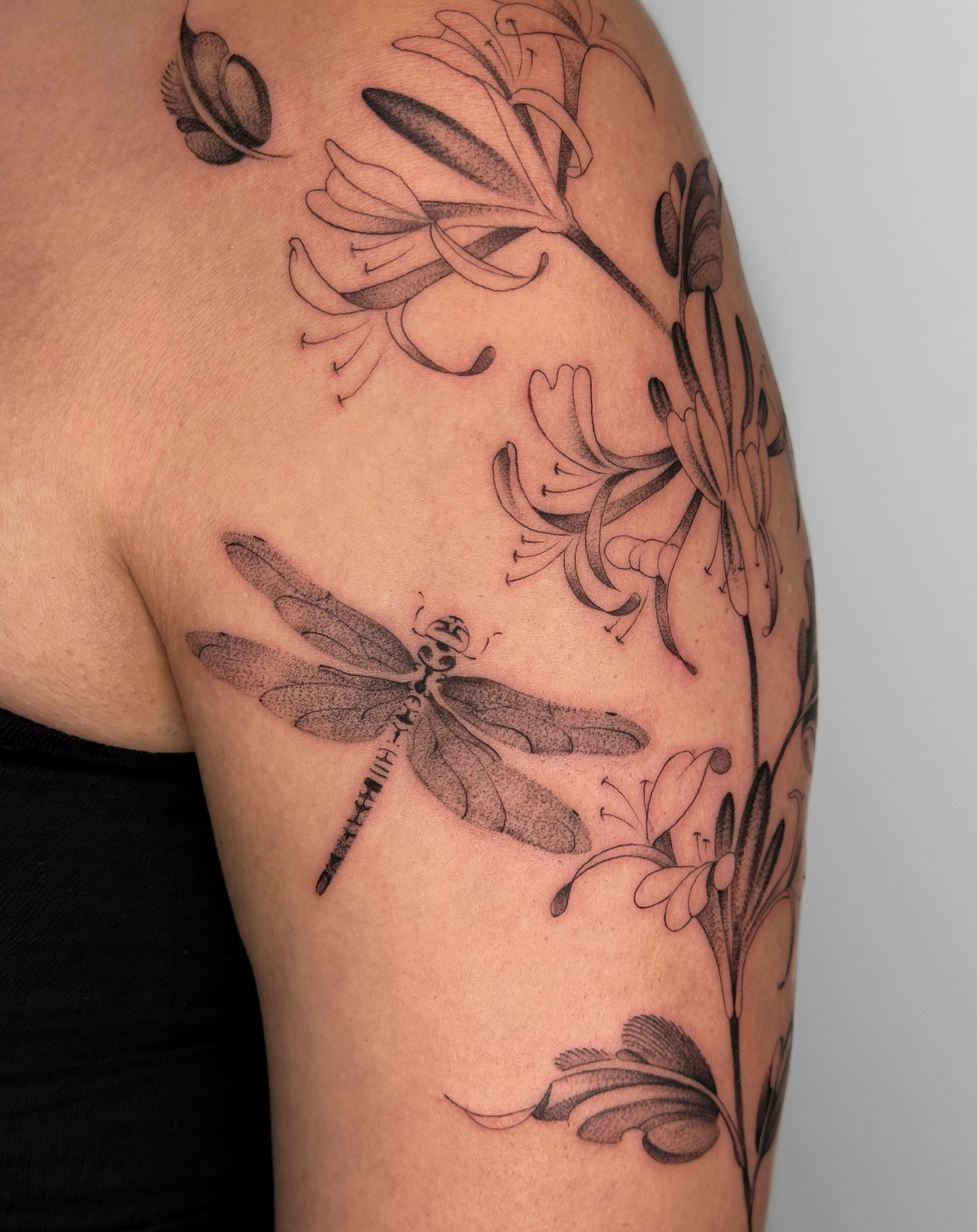 Dragonfly and flowers black and grey tattoo on the shoulder by Alyssa . Villela
