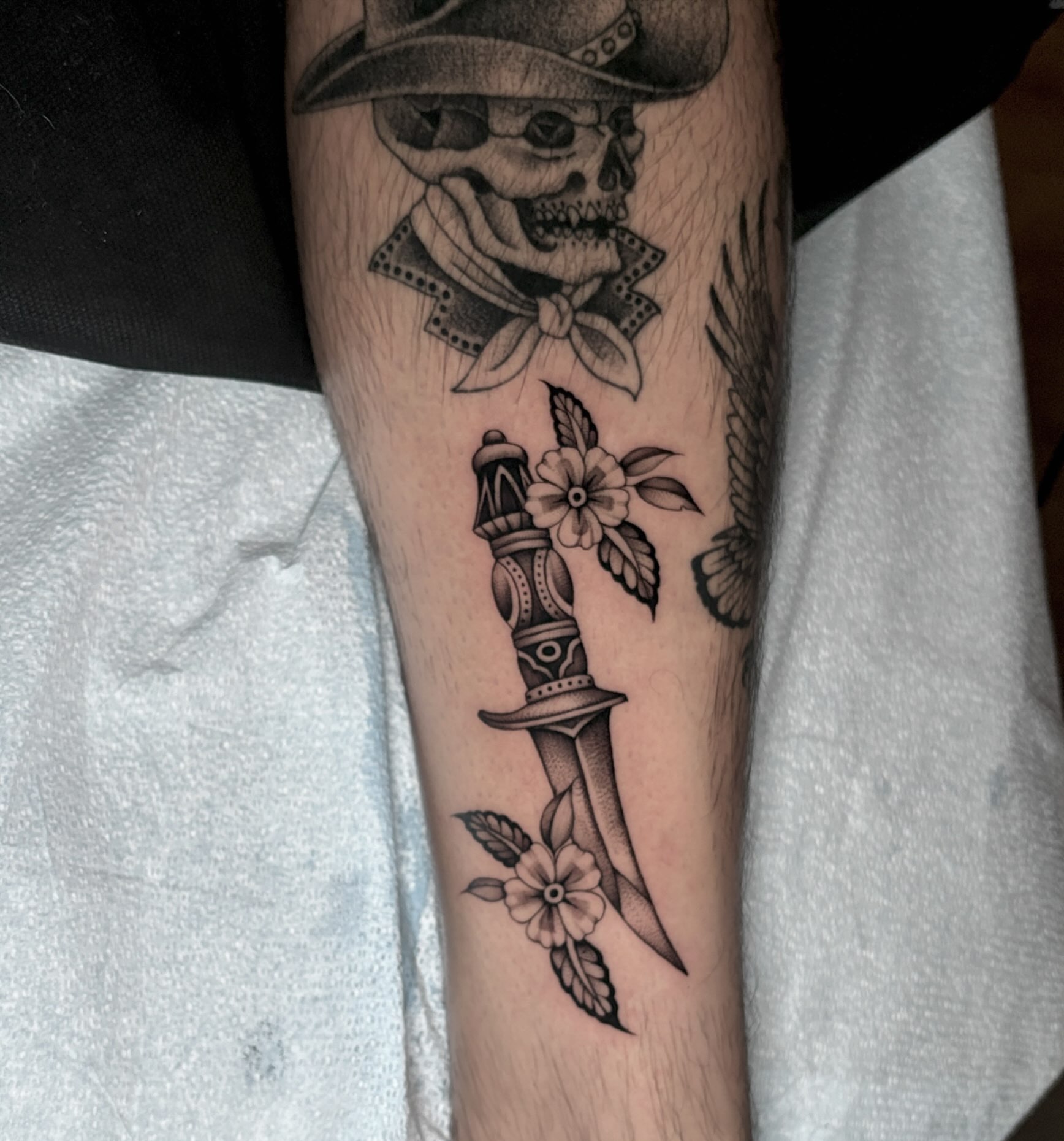 Knife and flowers black and grey tattoo on the forearm by Emma Cotter