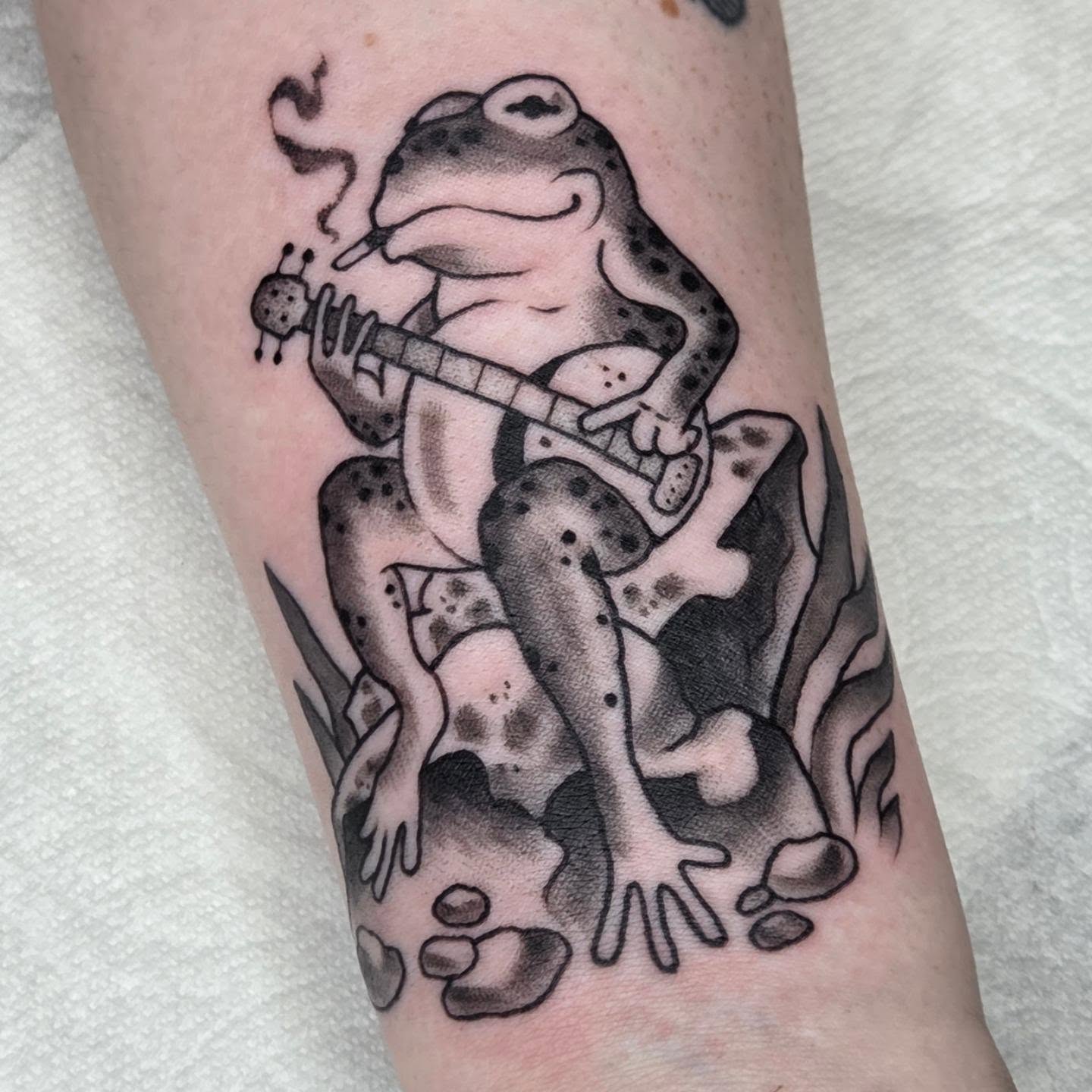 Frog playing guitar black and grey tattoo on the forearm by alec