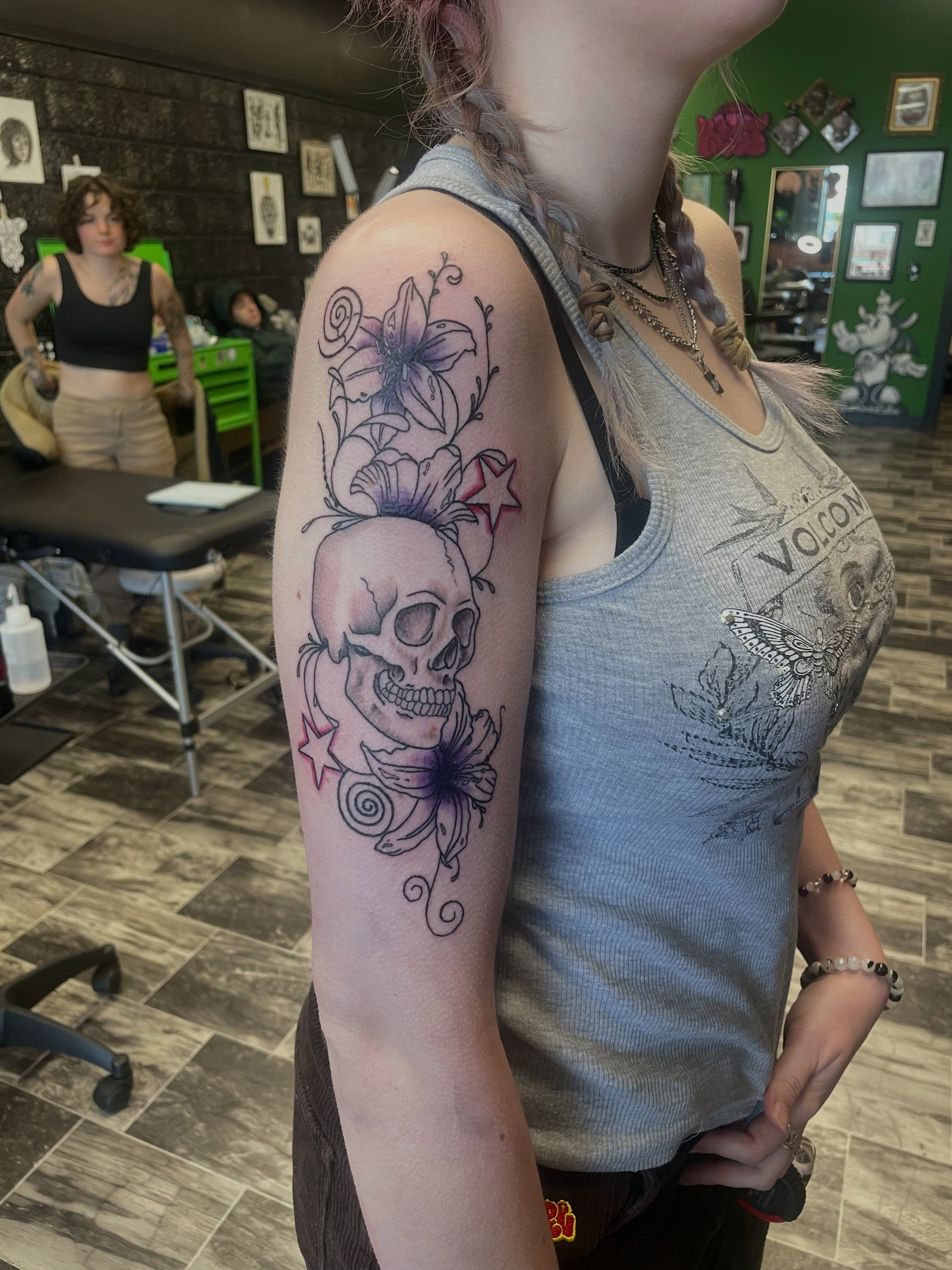 Skull with floral elements neo-traditional tattoo on the upper arm by Kaylee 🗡️