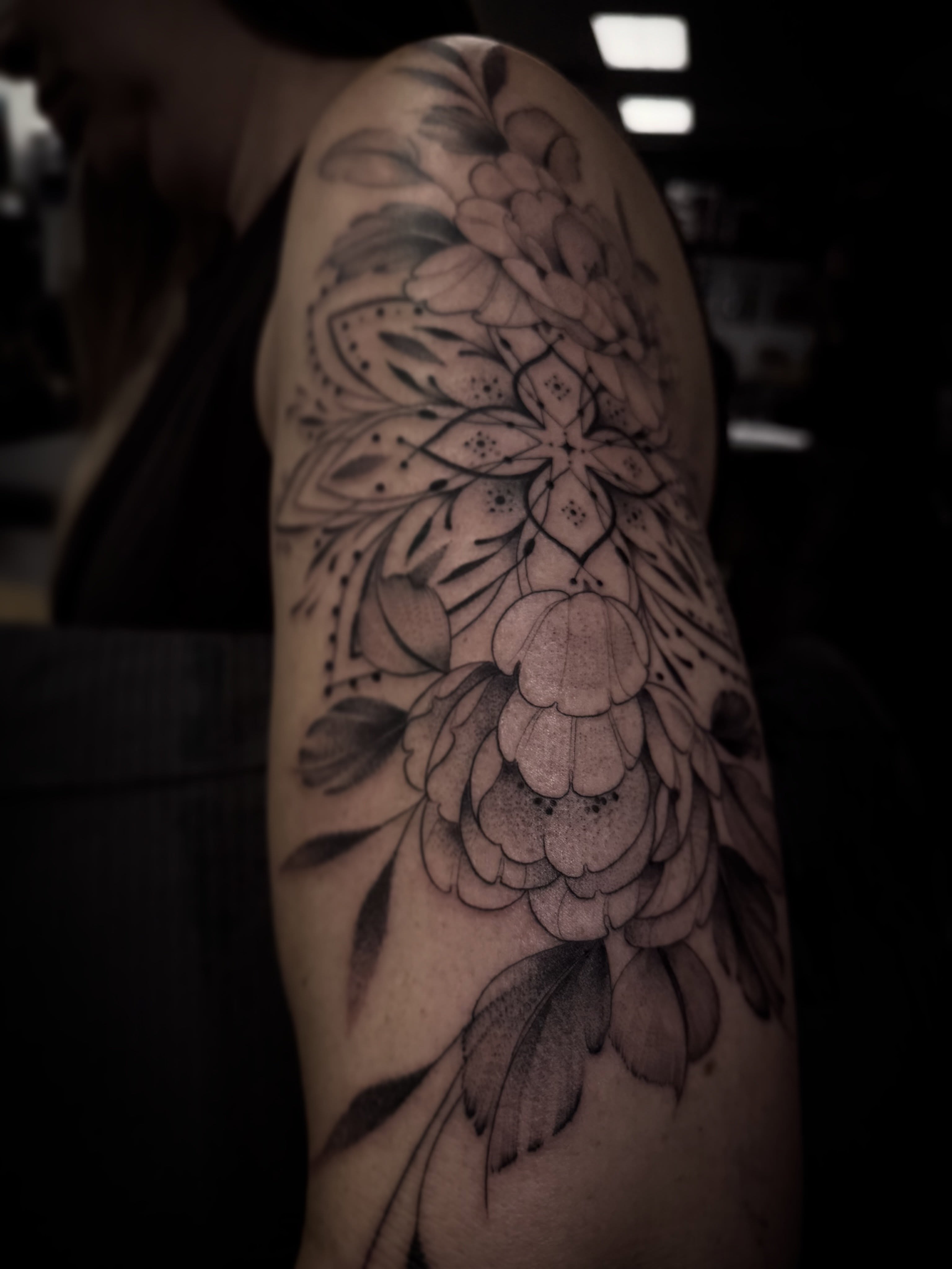 Floral arrangement black and grey tattoo on the upper arm by Chloe