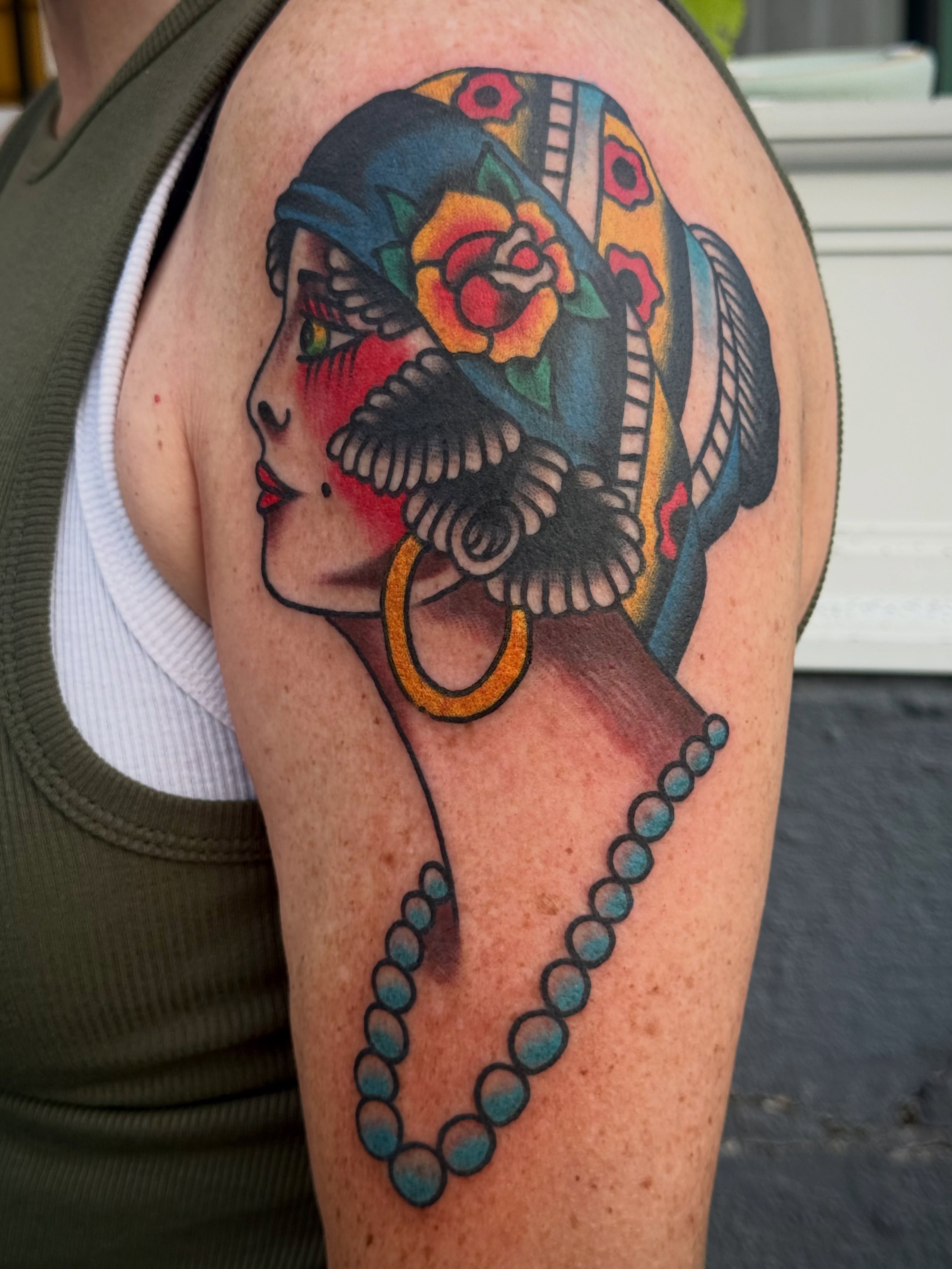 Woman with floral headdress American traditional tattoo on the shoulder by Chuck Derek Whitaker