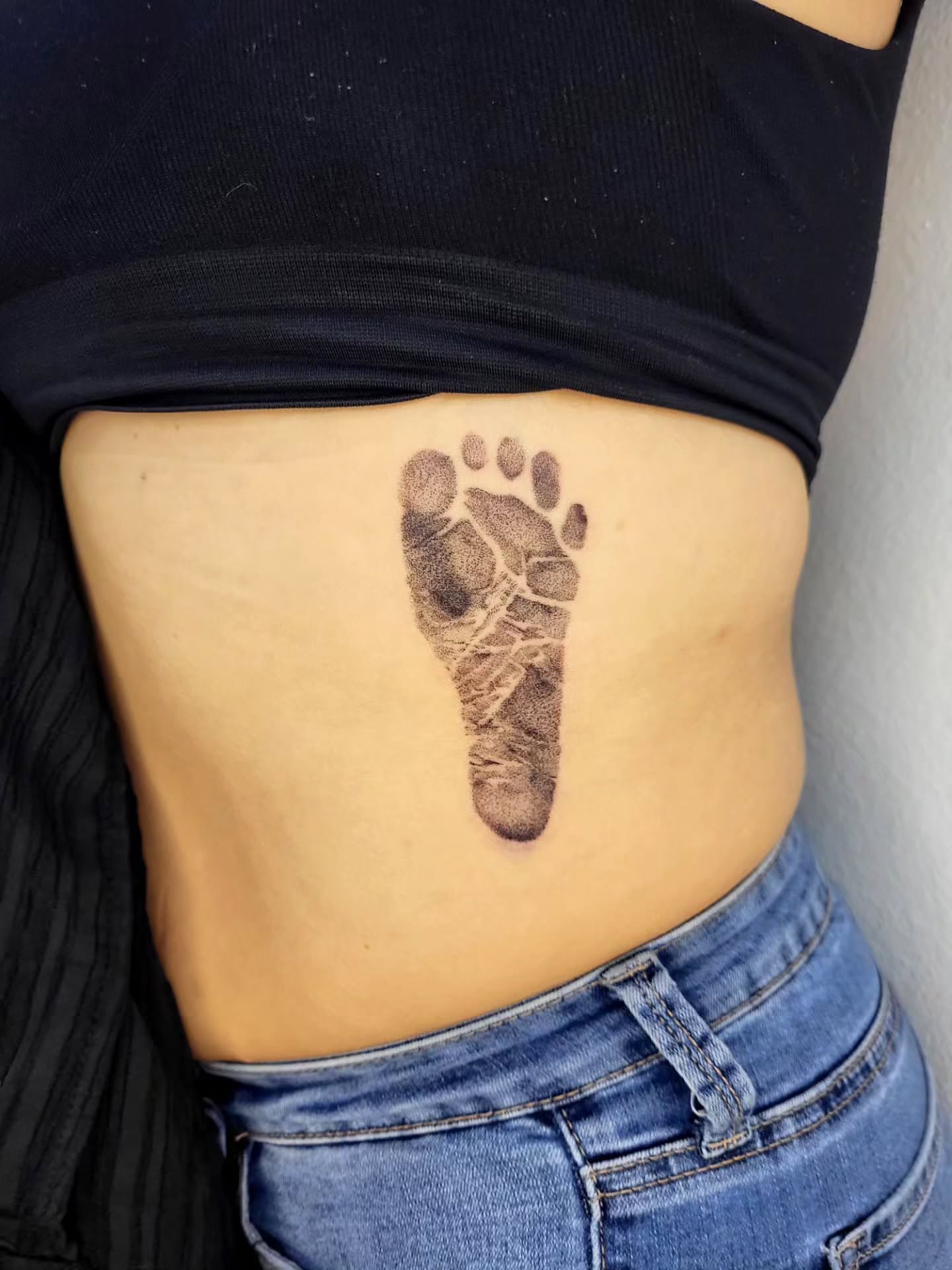 Footprint black and grey tattoo on the torso by 𝓥𝓮𝓰𝓪𝓼 𝓣𝓪𝓽𝓽𝓸𝓸 𝓐𝓻𝓽𝓲𝓼𝓽