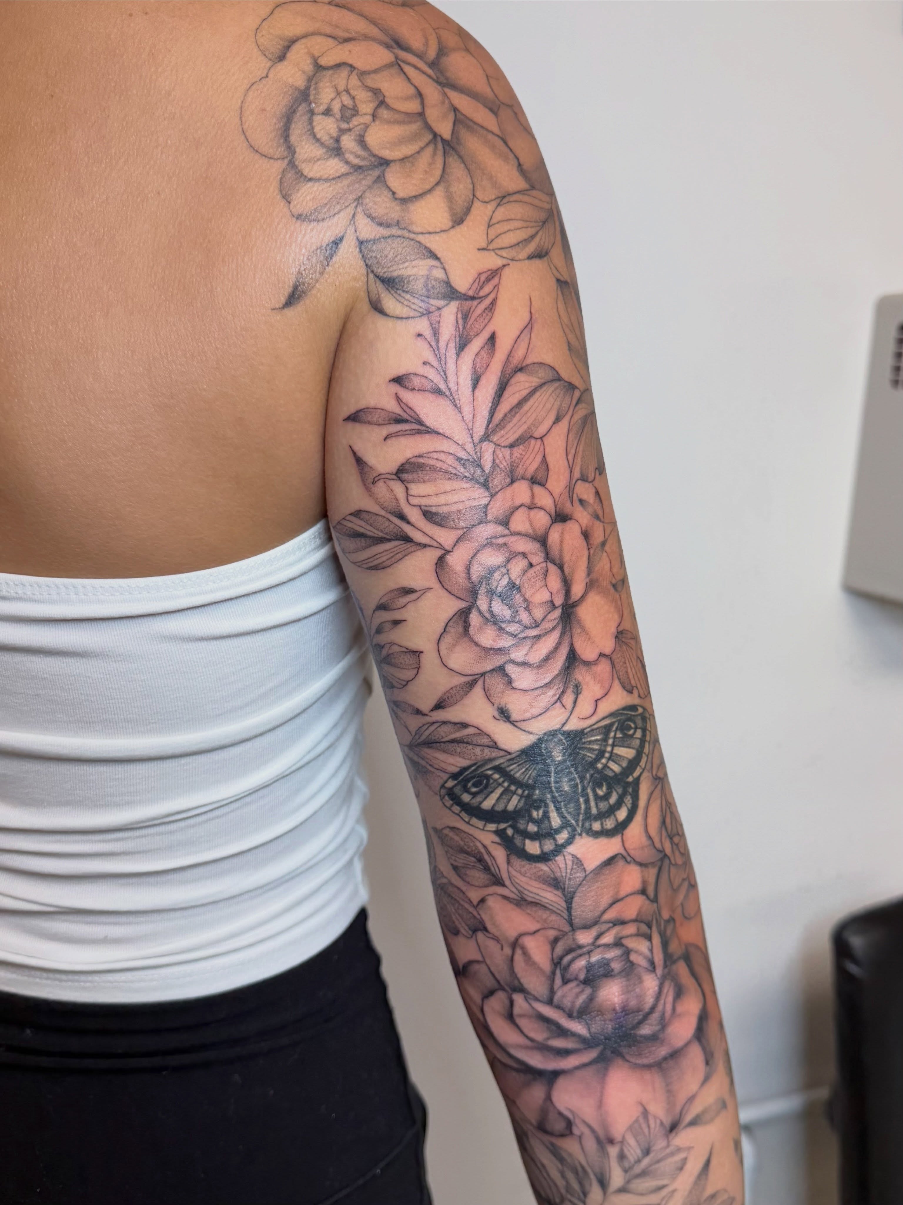 Flowers and butterfly black and grey tattoo on the upper arm by Bridget Smith