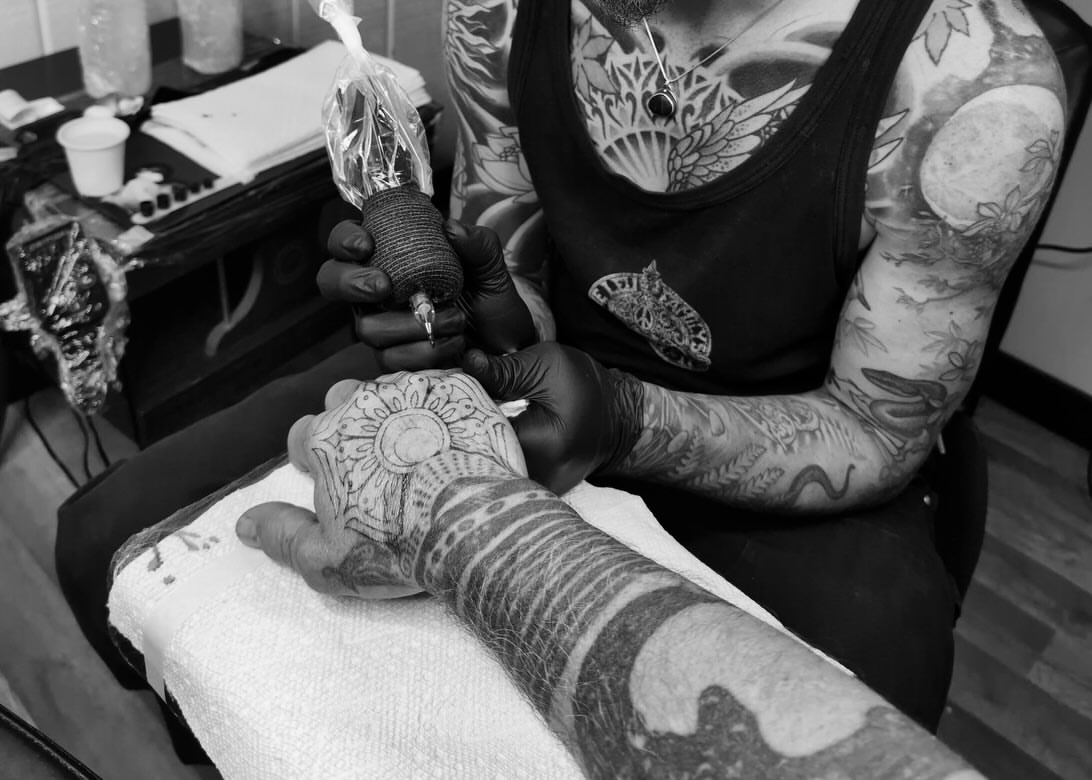 Sun and floral pattern black and grey tattoo on the forearm by Owlyn Madrone