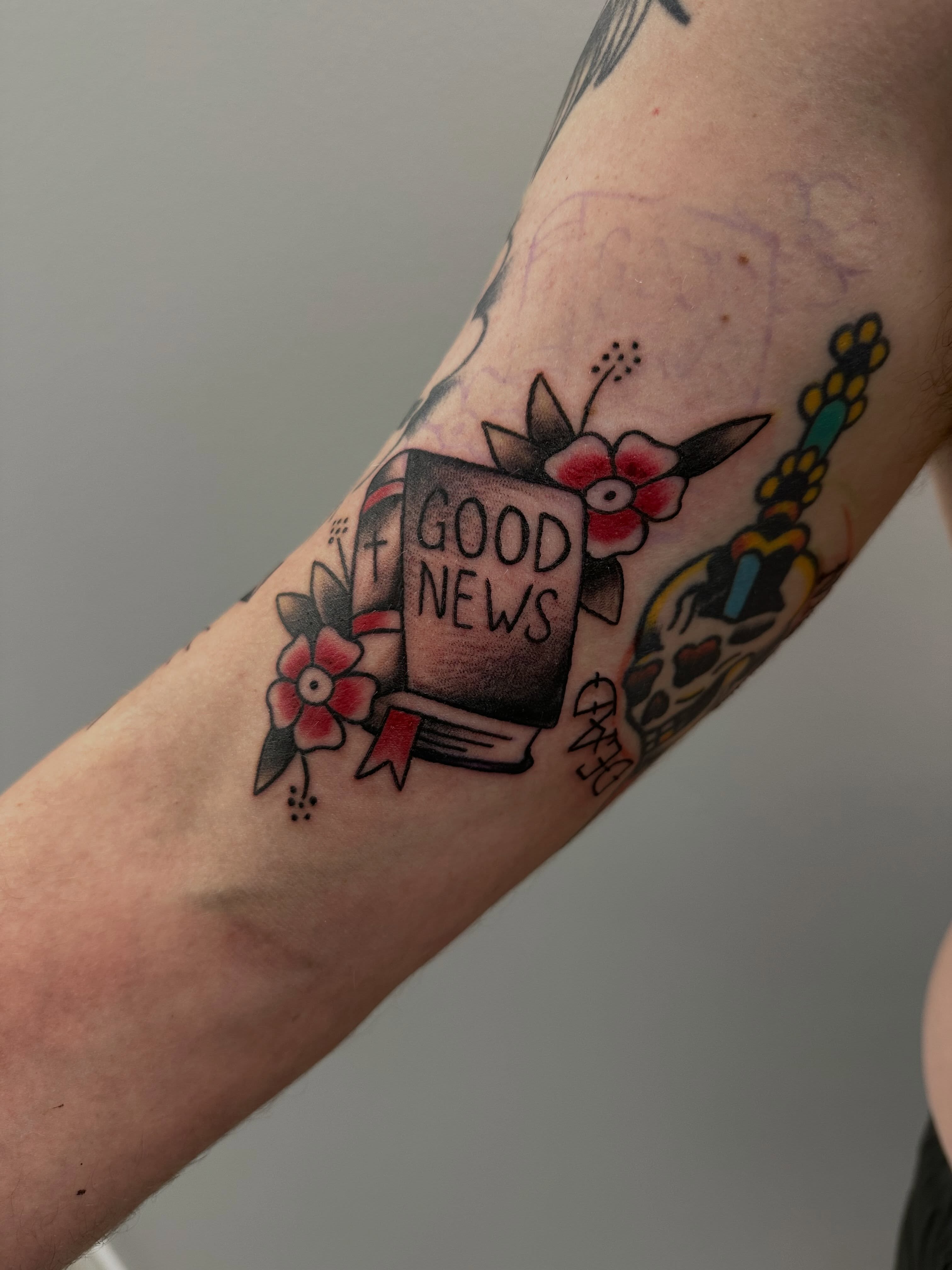 Book with 'GOOD NEWS' American traditional tattoo on the forearm by Vincent Merys