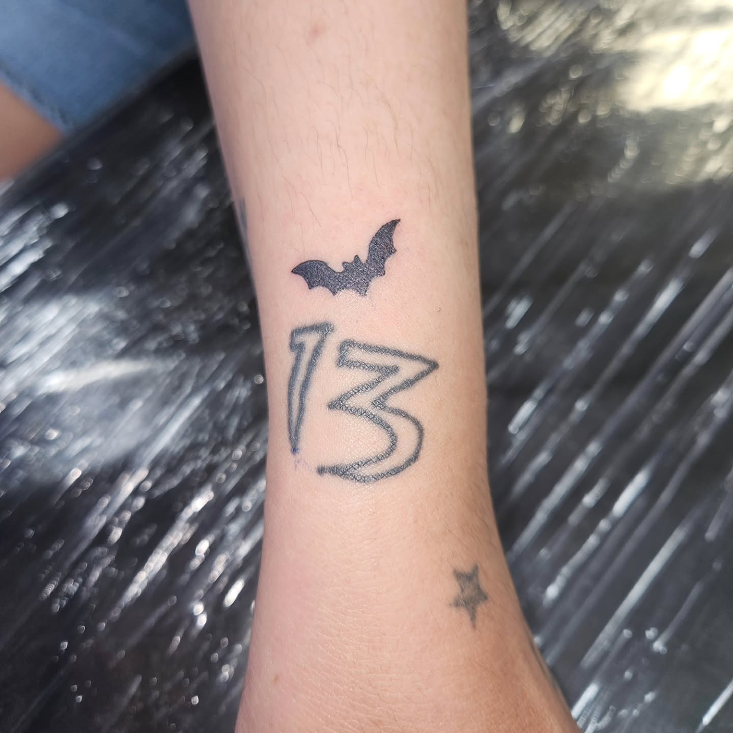 Bat and number 13 black and grey tattoo on the forearm by Mischief π€