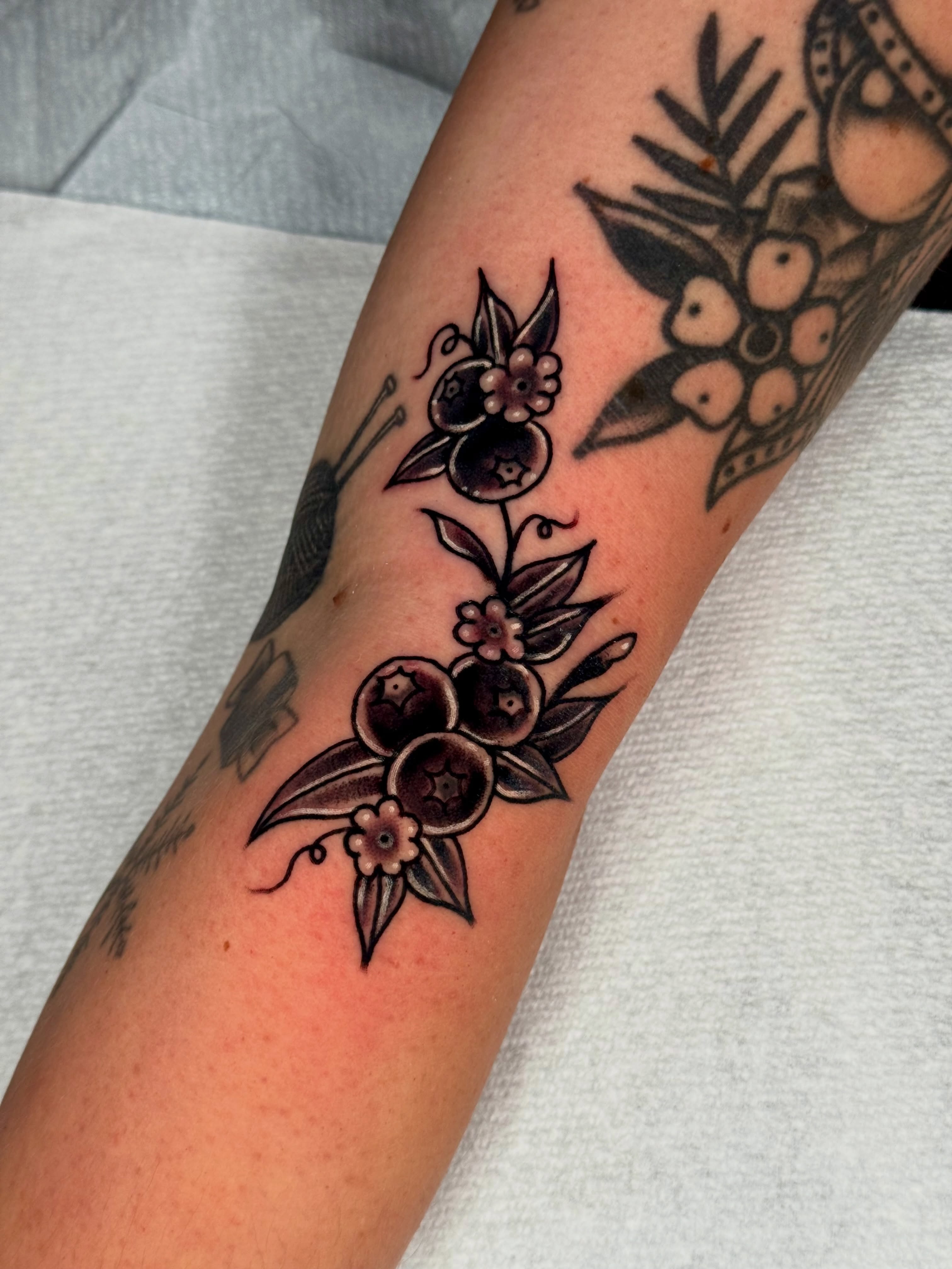 Blueberries and flowers black and grey tattoo on the forearm by Joe Bear Tattooer