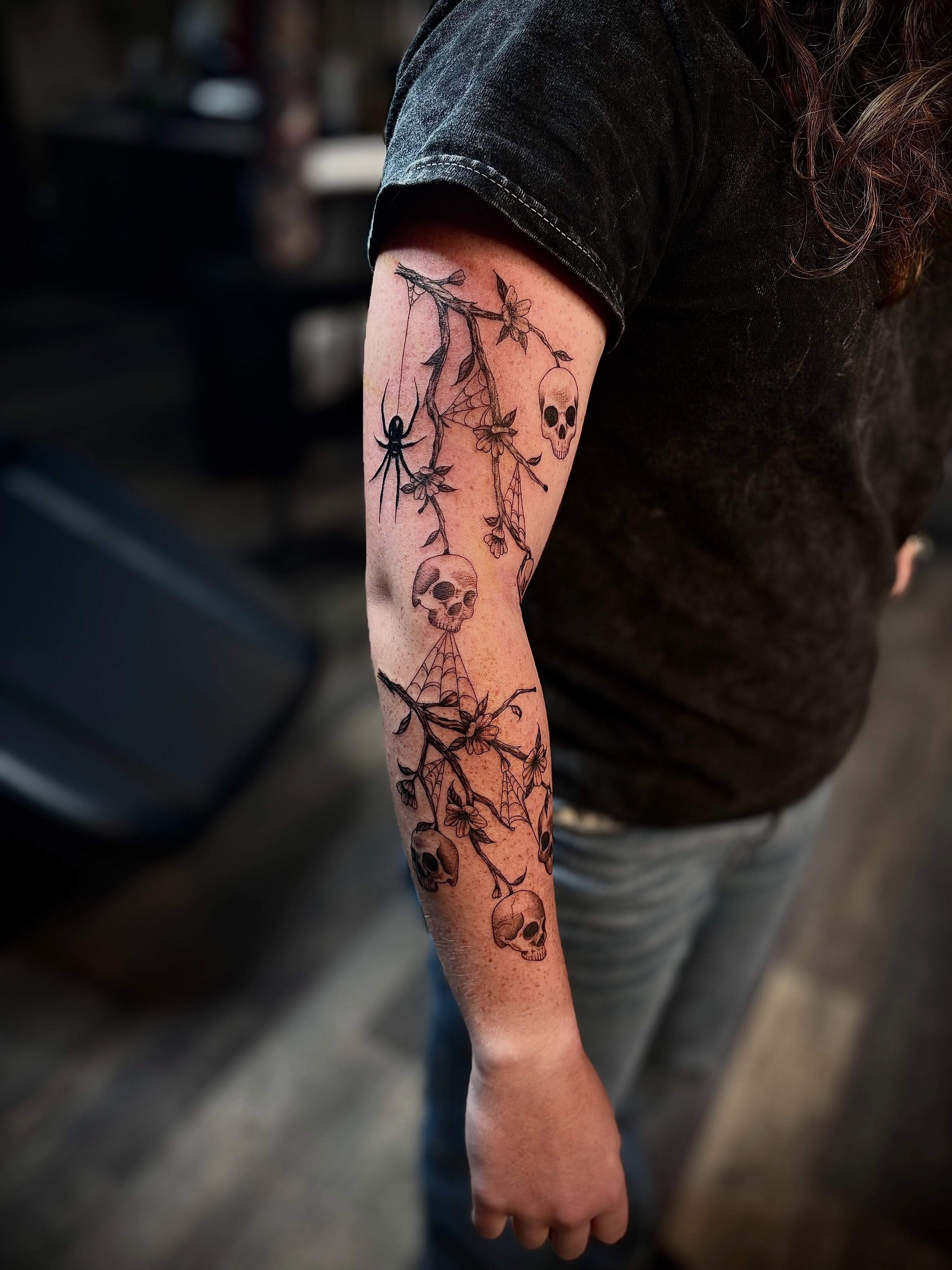Skulls and spider webs black and grey tattoo on the forearm by Tessa Simmons - Tattoo Artist