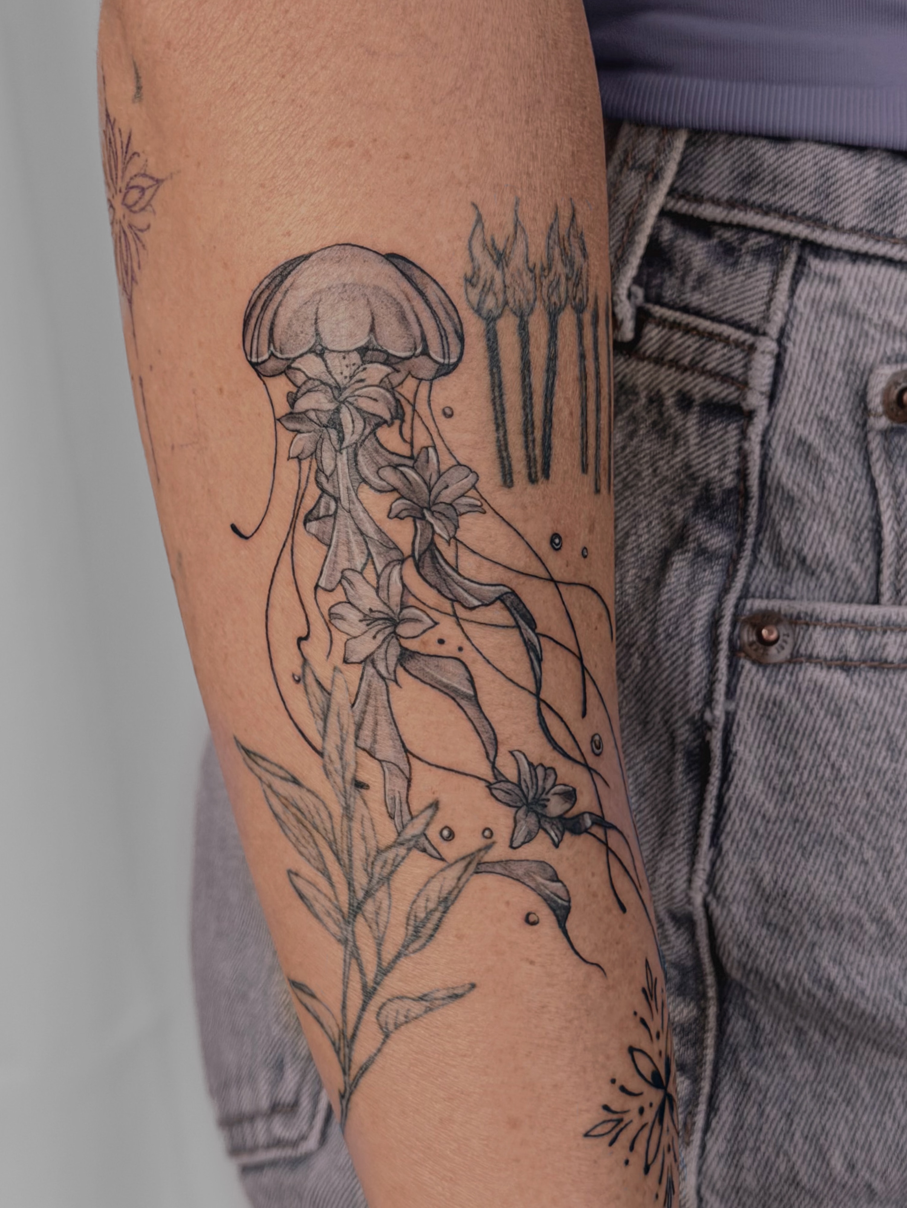Jellyfish and flowers black and grey tattoo on the forearm by Charlotte