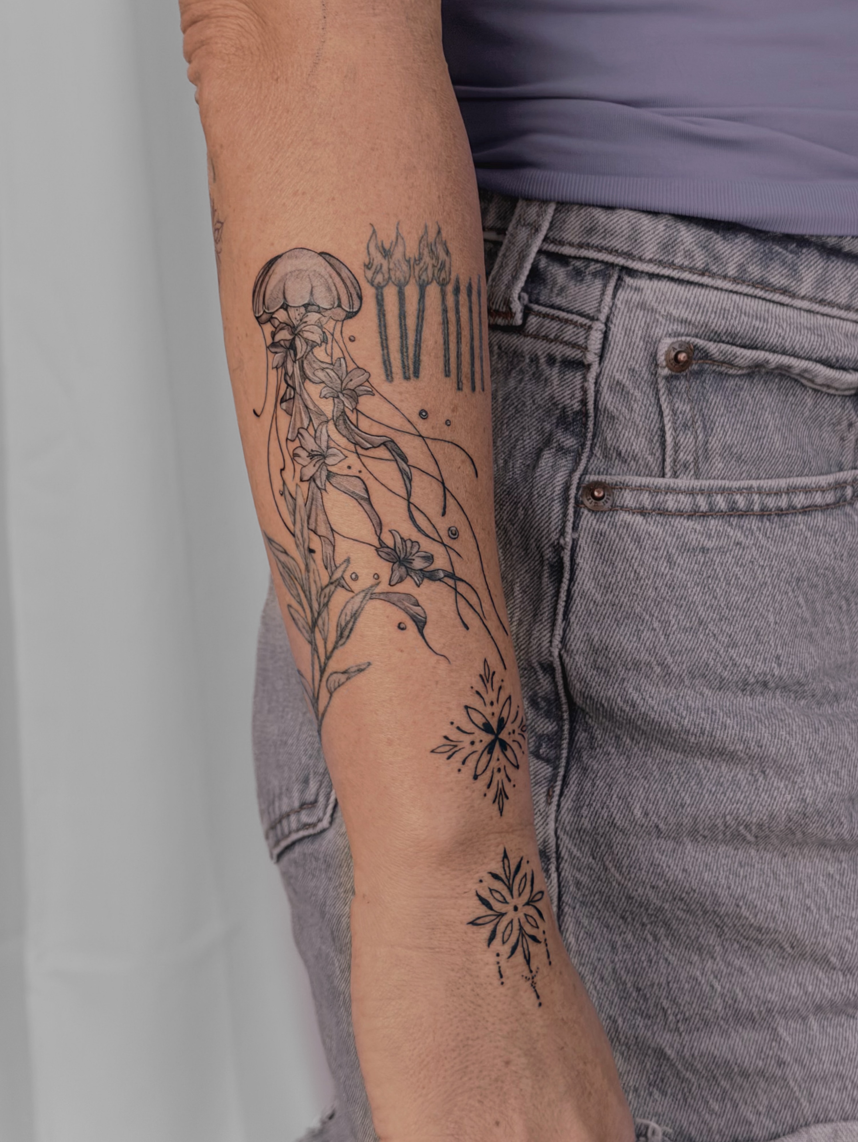 Jellyfish and flowers black and grey tattoo on the forearm by Charlotte