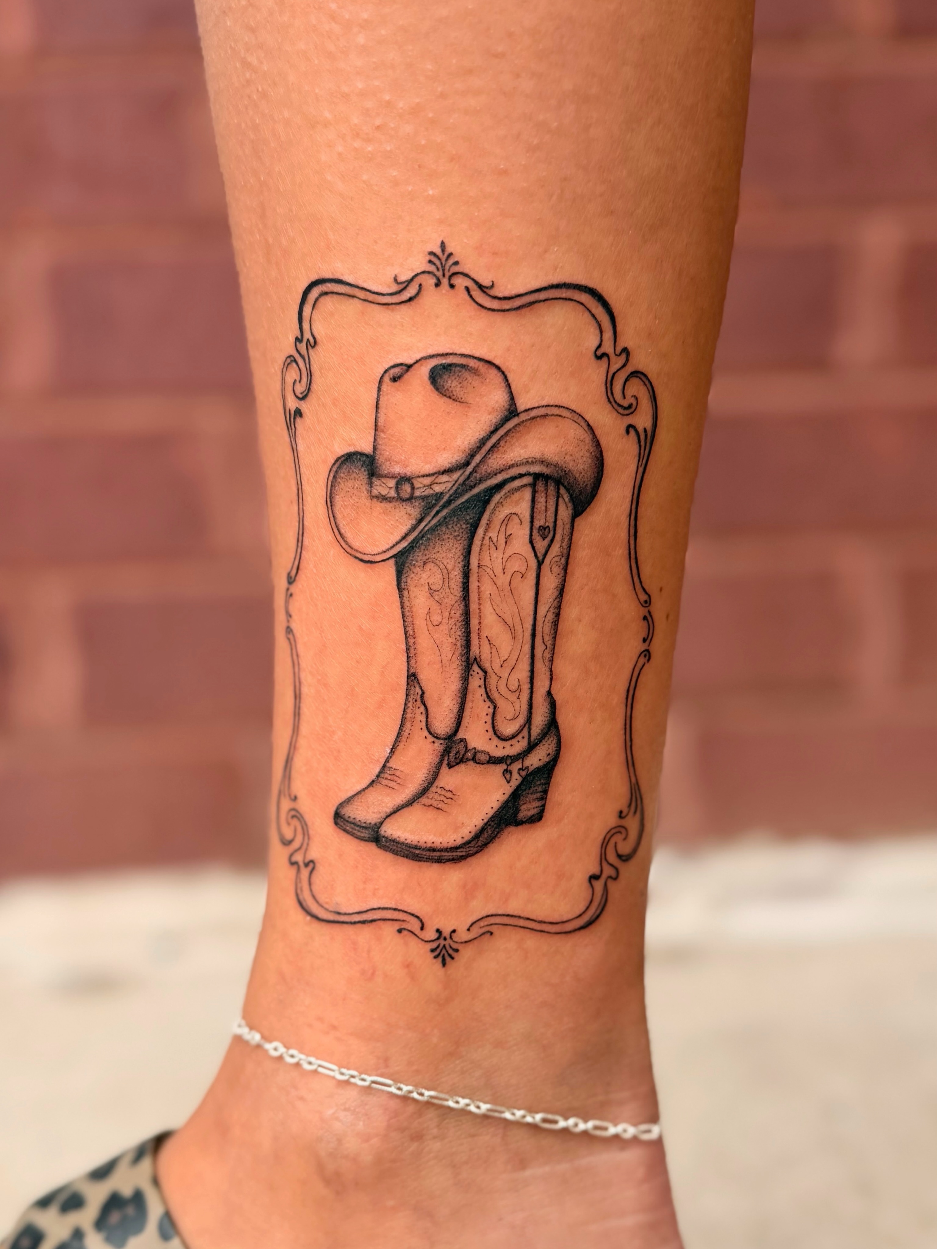 Cowboy boots and hat black and grey tattoo on the forearm by Emily Velletta, Huntersville, North Carolina