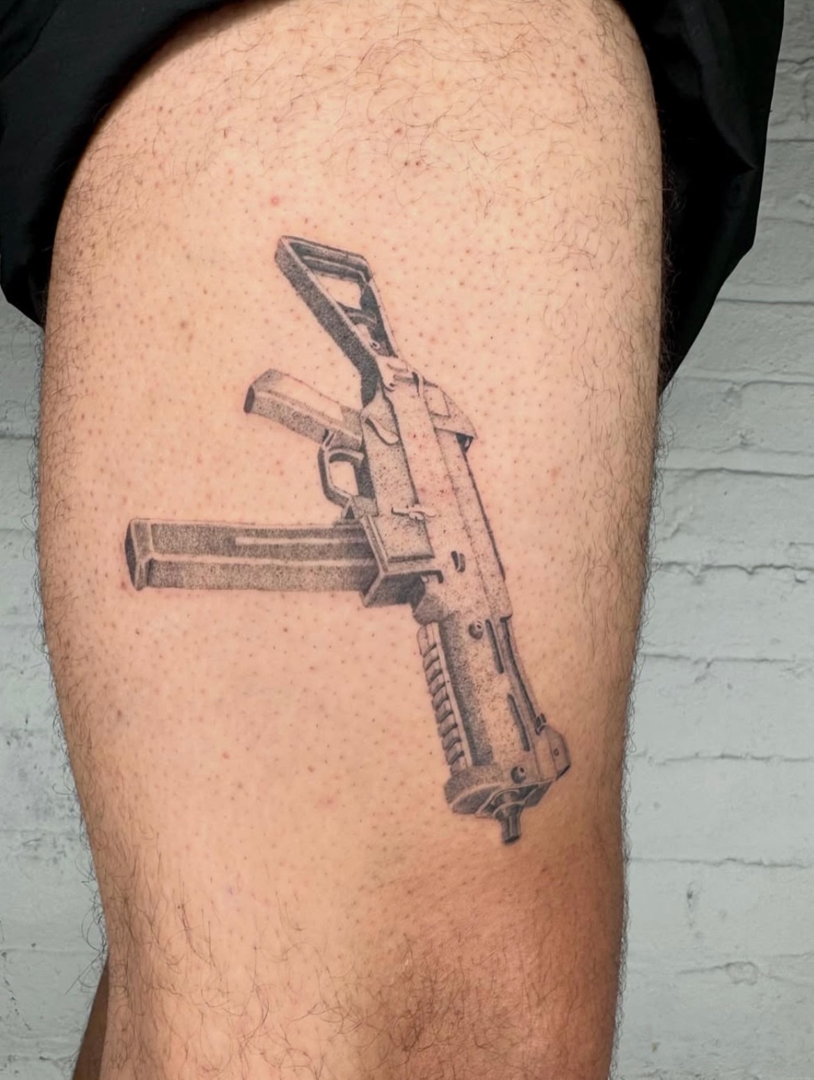 Machine gun black and grey tattoo on the thigh by Kenny ๐ด