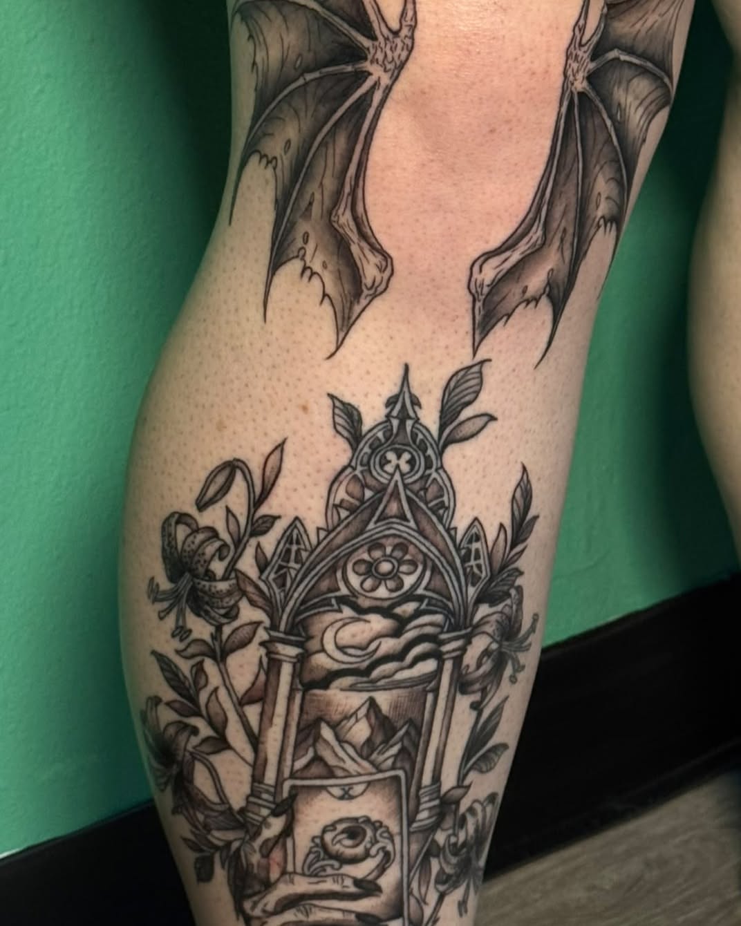 Gothic archway with bat wings dark realism tattoo on the thigh by Sabrina